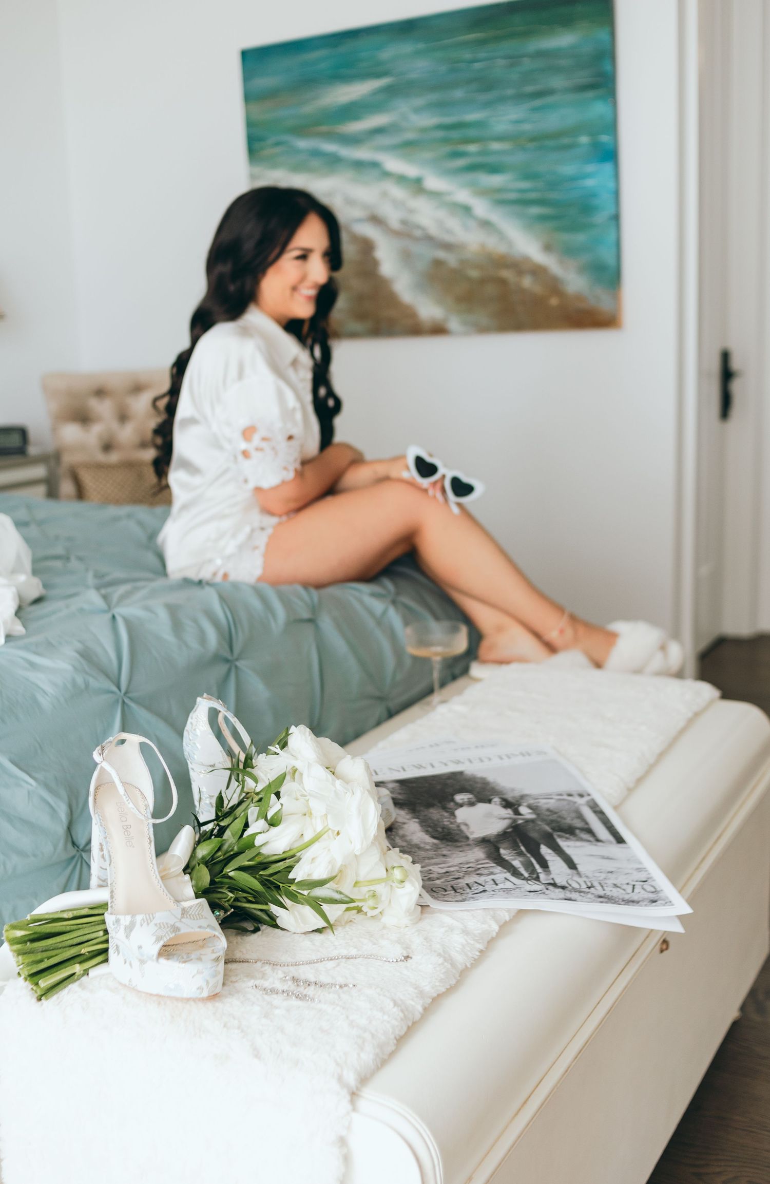 Wedding details including white bouquet and shoes with a beach painting in background.