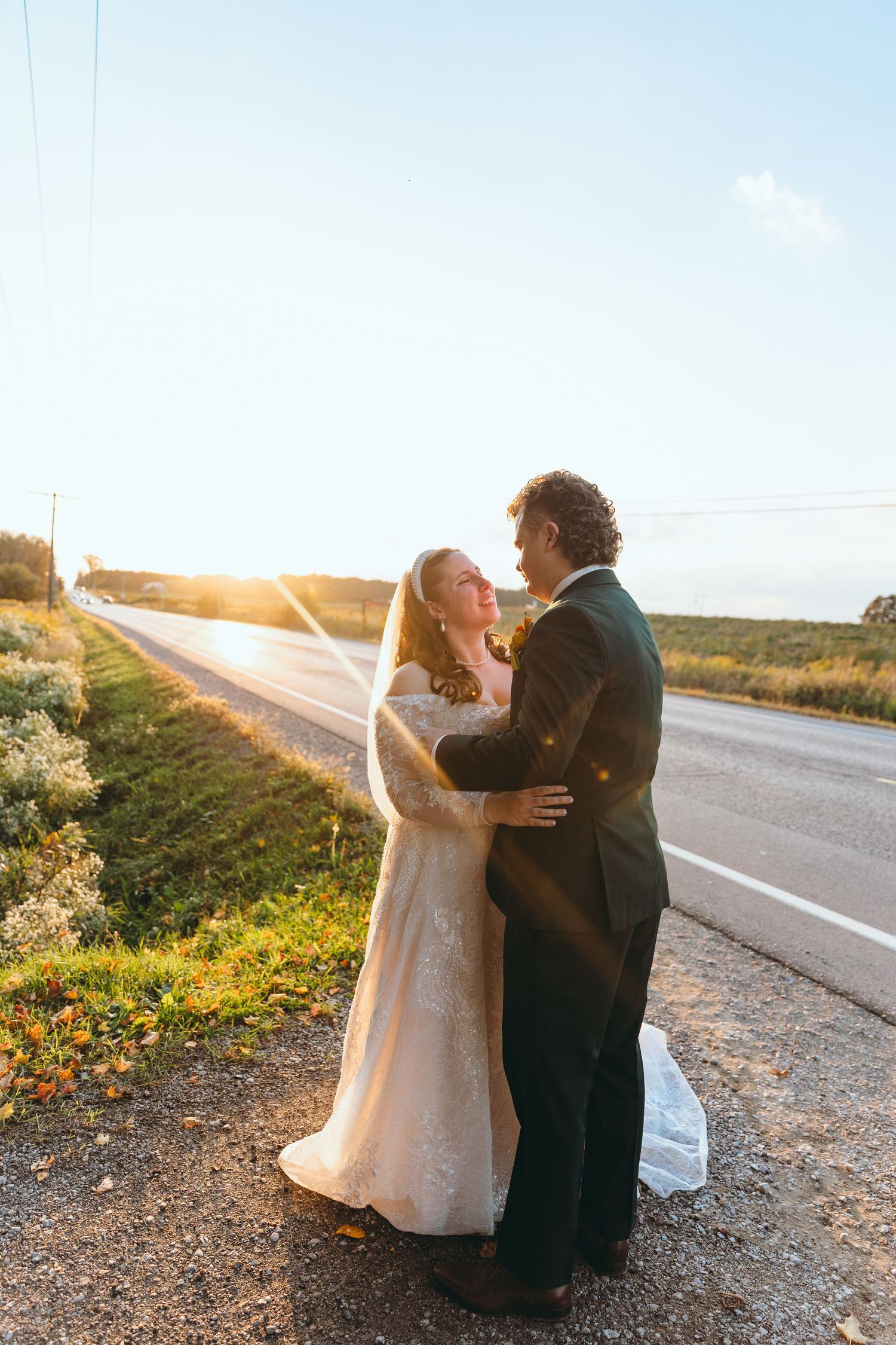 Couple sits together on roadside during golden hour wedding photoshoot.