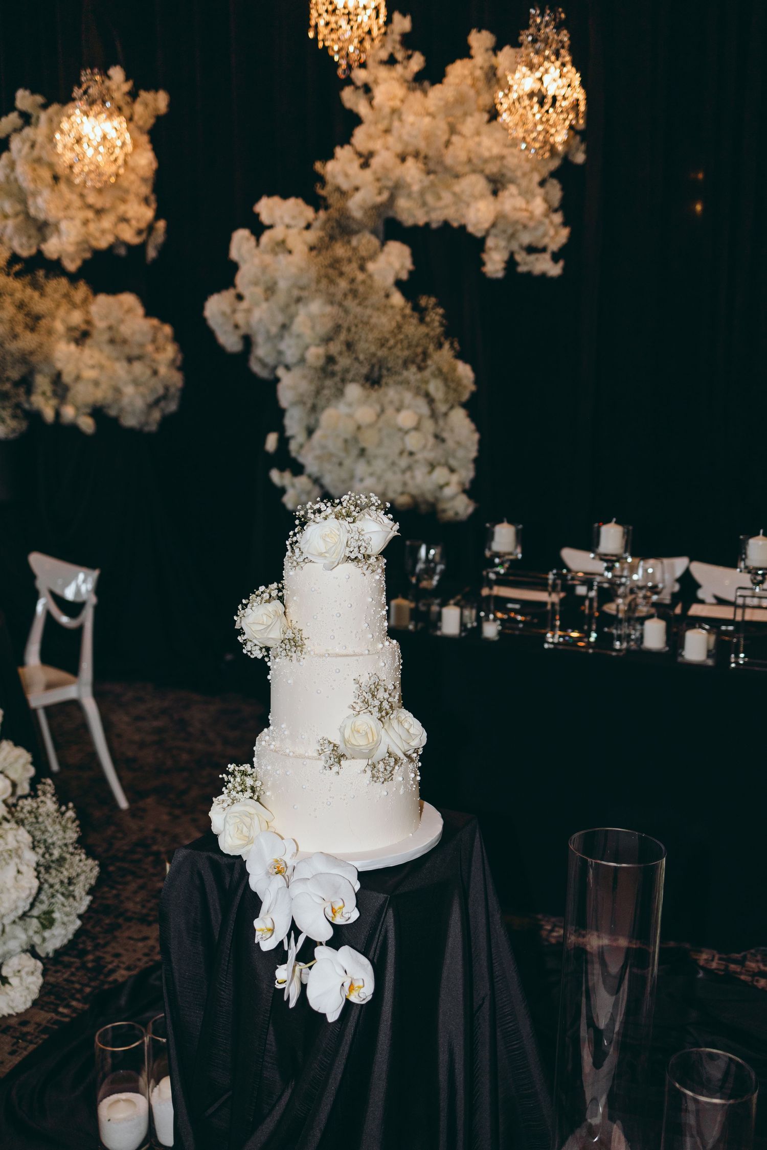Elegant white wedding cake with floral decorations under cloud-like hanging installations.