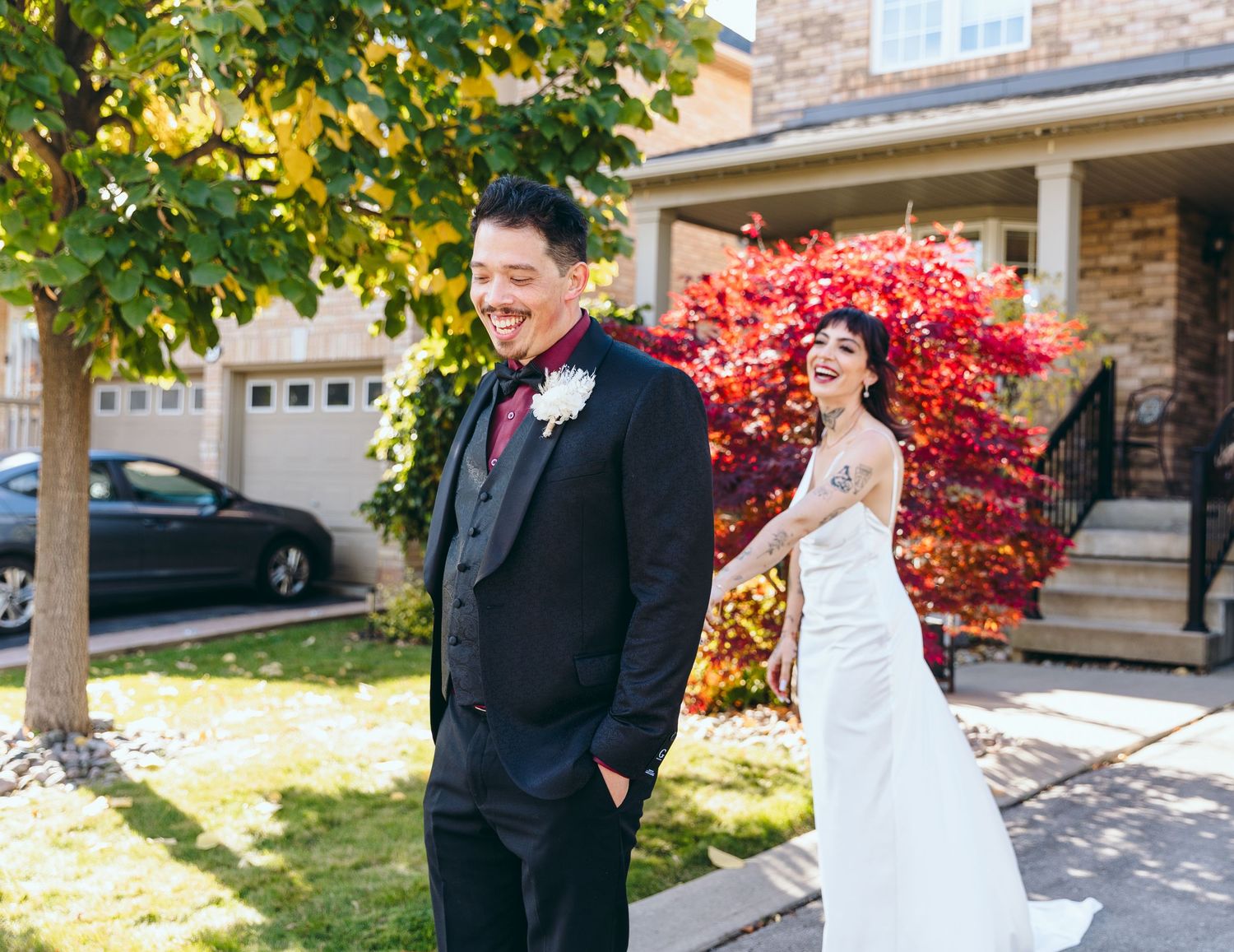 Wedding couple sharing a first look moment in front of a house with autumn foliage.