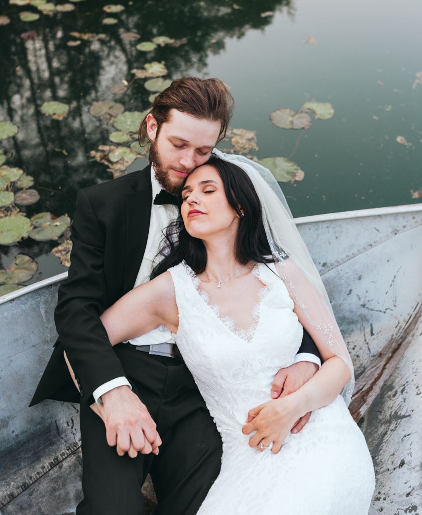 Tender moment between newlyweds in boat surrounded by lily pads on peaceful lake.