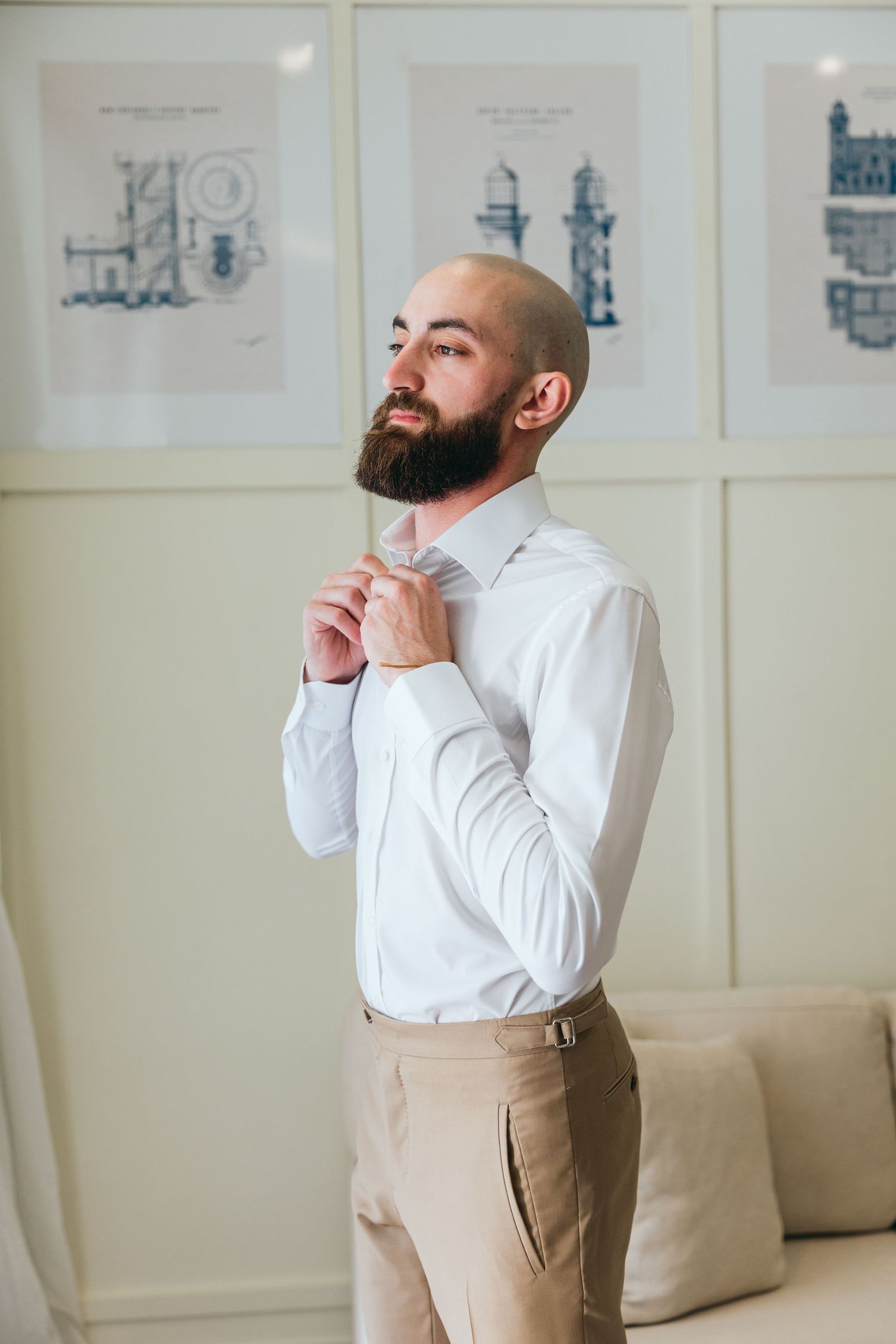 A person in formal attire adjusting their tie while standing in a room with framed artwork.