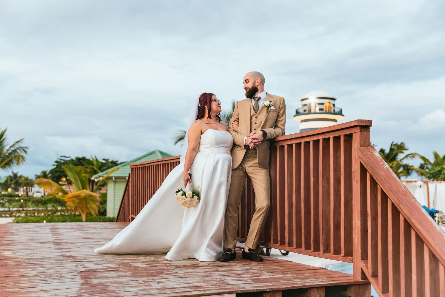 Wedding couple posing on a wooden deck with tropical scenery and palm trees in the background.