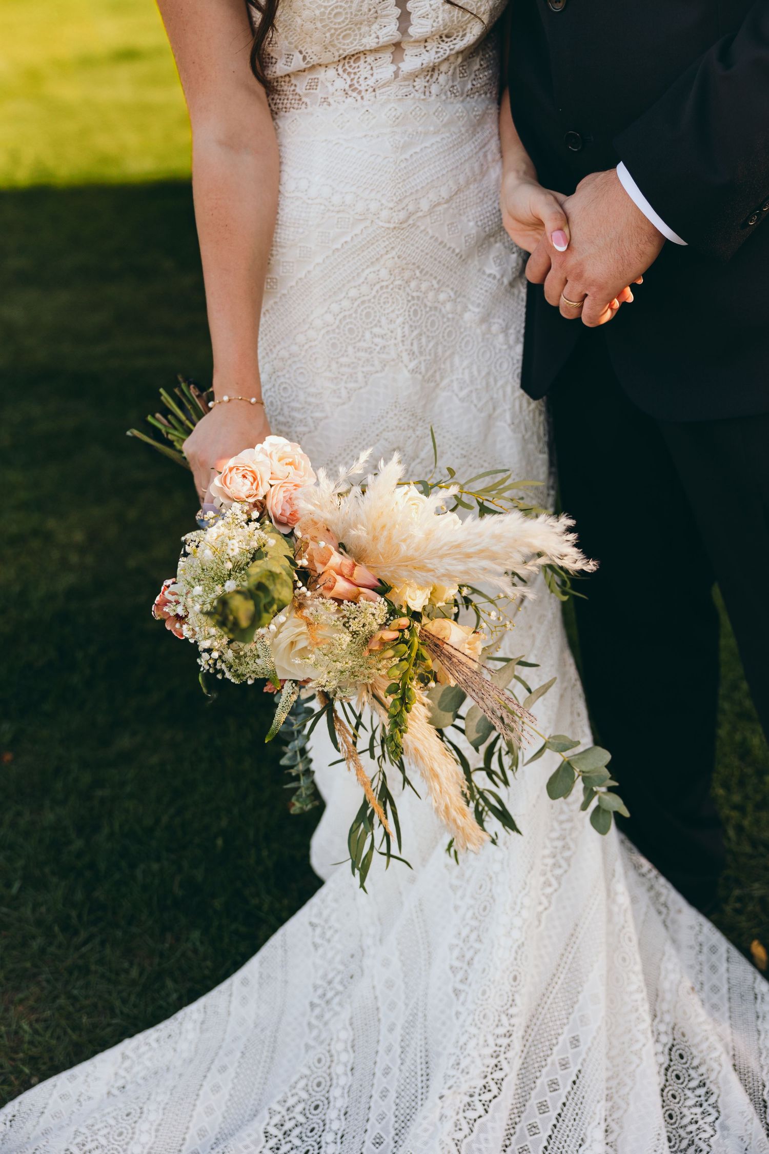Close-up of a delicate bridal bouquet with peach and white flowers against a lace wedding dress.