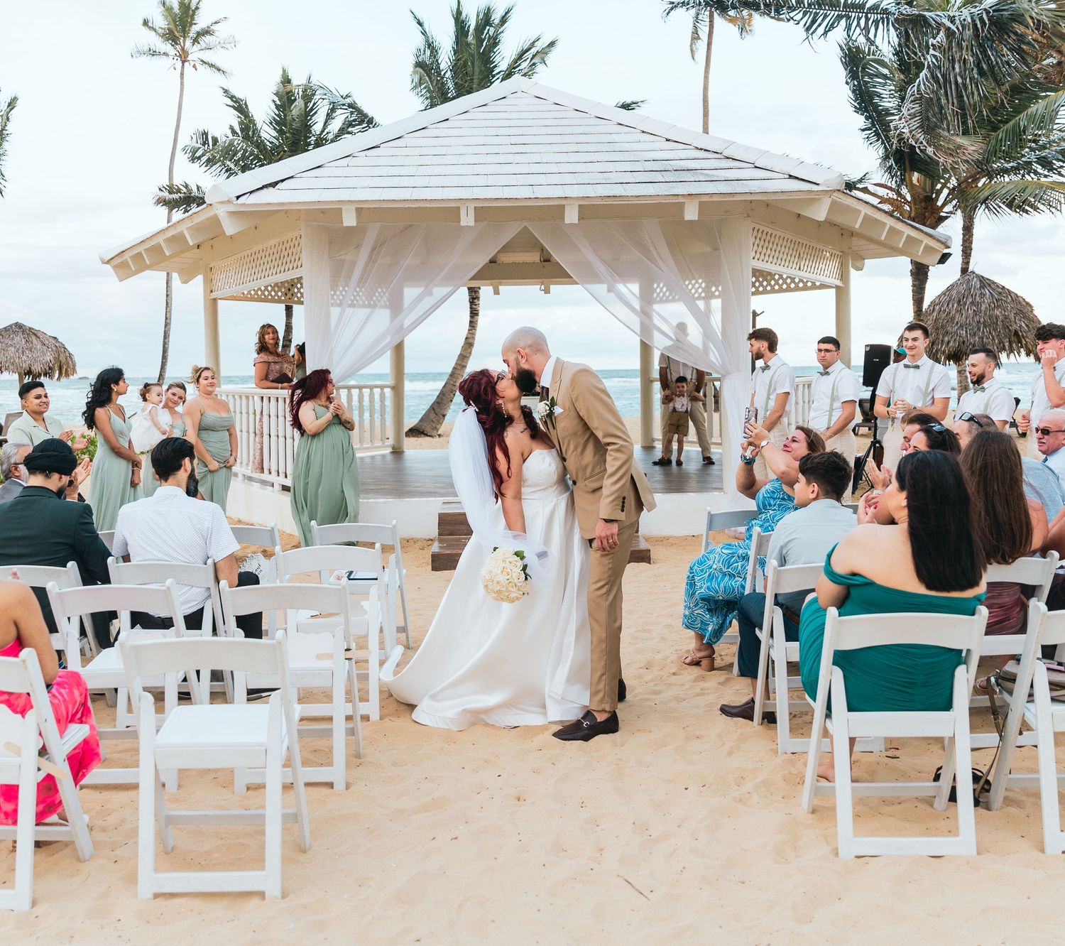 Panoramic view of a beach wedding setup with white gazebo and palm trees along the shoreline.