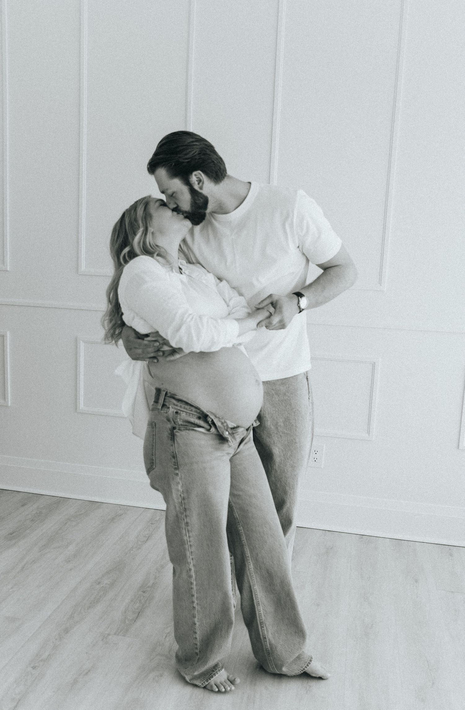 Intimate maternity photos of couple embracing in casual white and denim outfits.