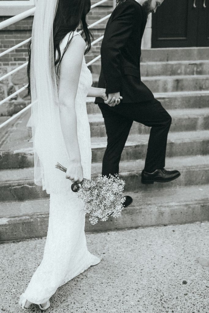 Black and white photo of wedding dress details and feet walking up concrete stairs.