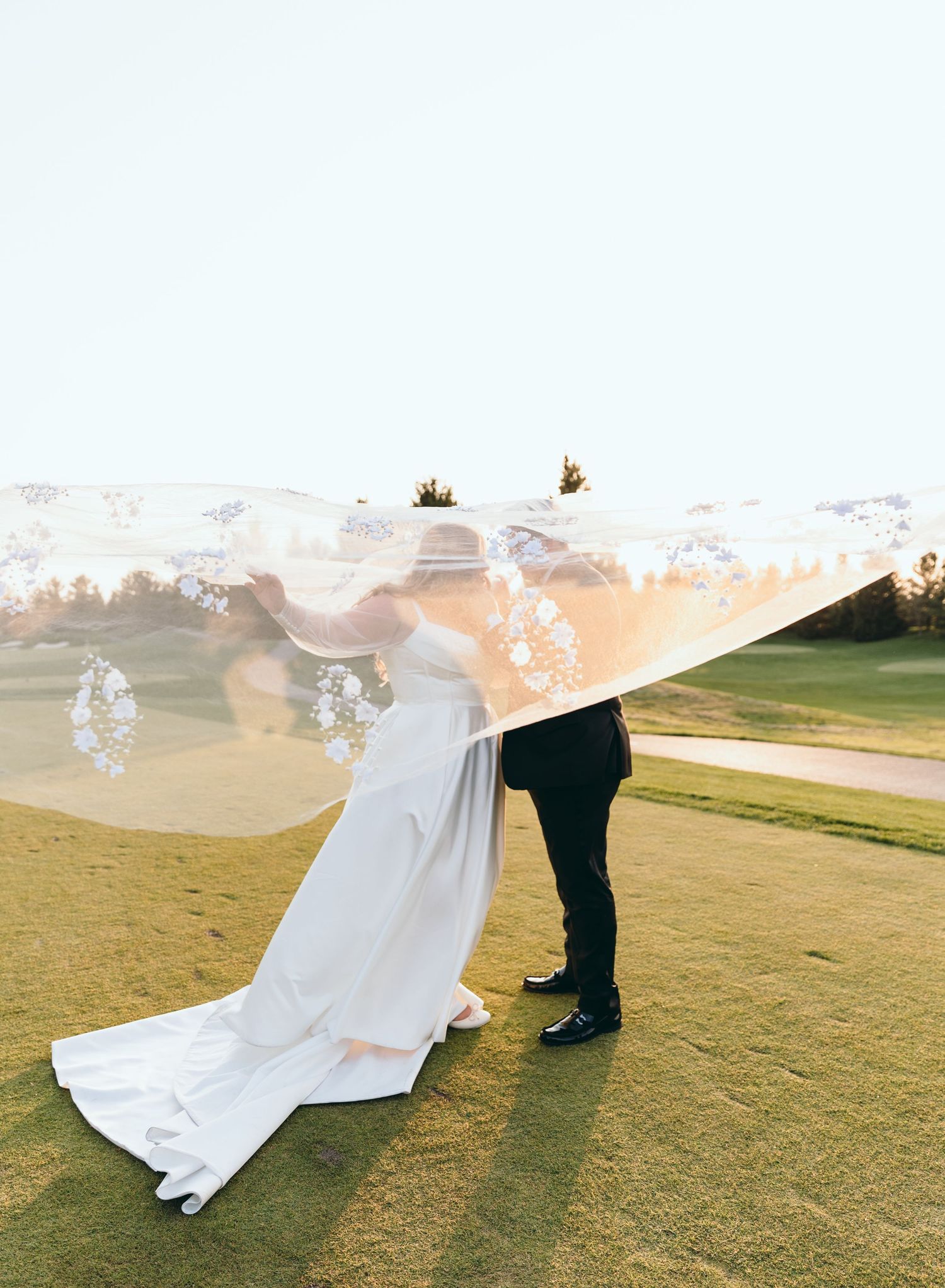 Romantic wedding photo with flowing veil on golf course at sunset.