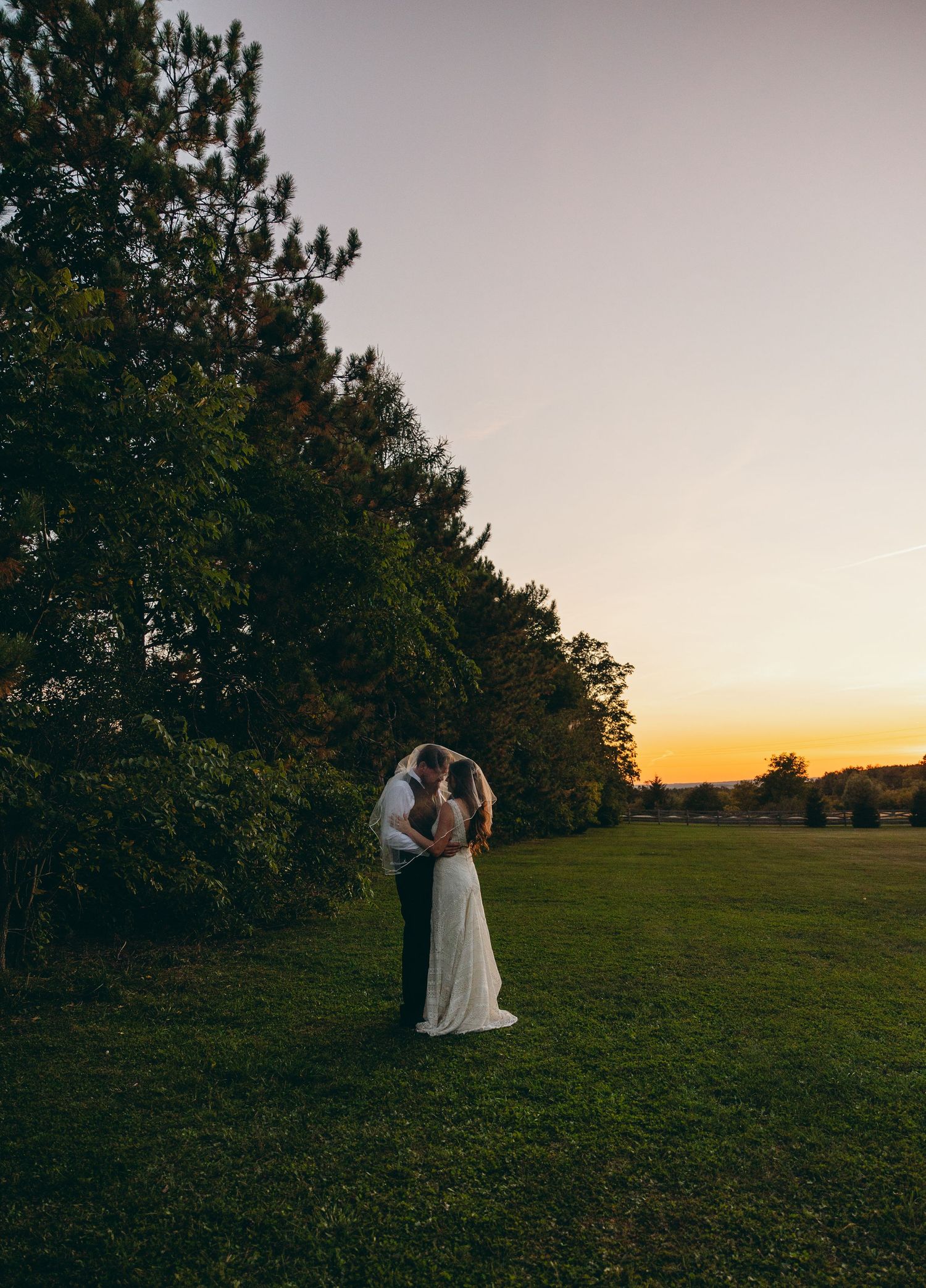 Silhouettes of two people standing on a grassy hill at sunset.