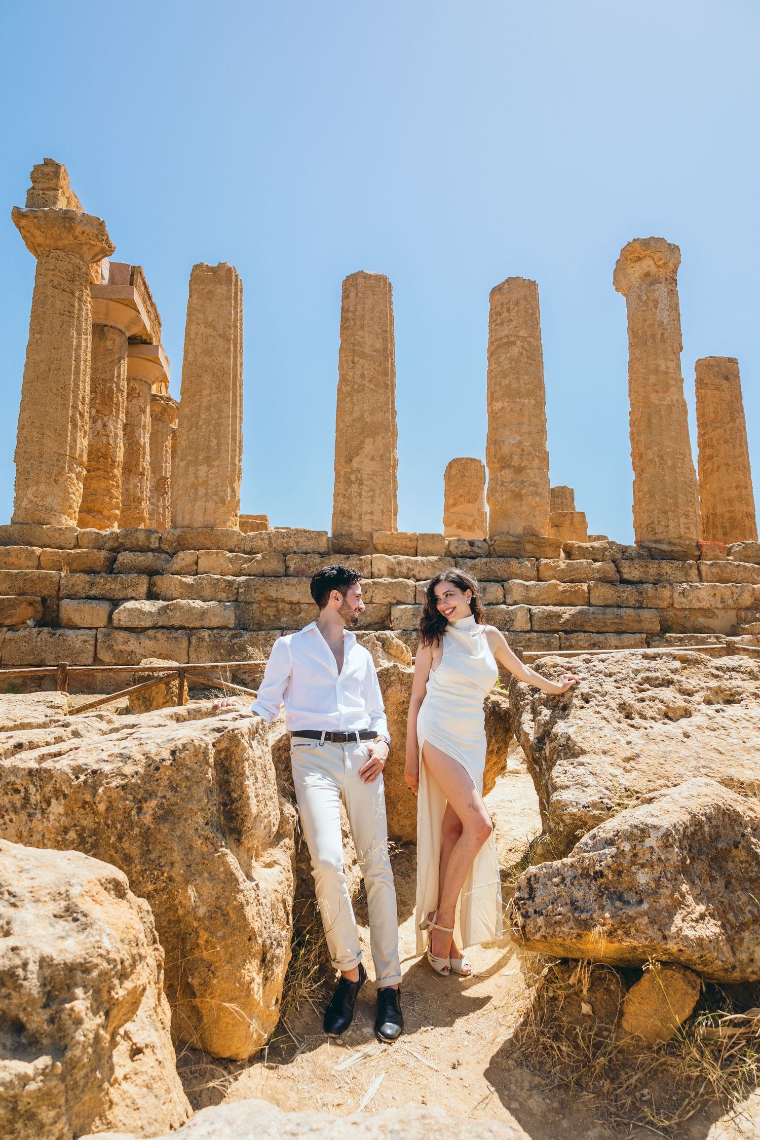 A couple poses romantically among ancient Greek temple ruins with tall stone columns in the background.