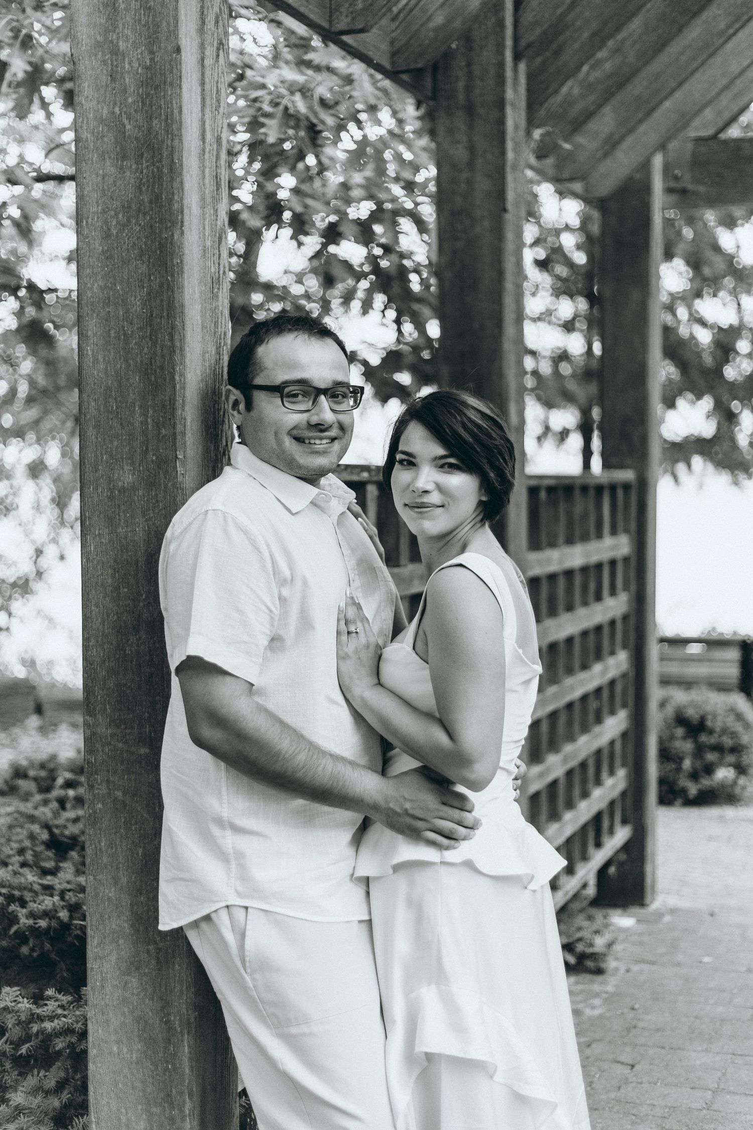 Couple in white outfits sharing intimate moment under wooden covered walkway.