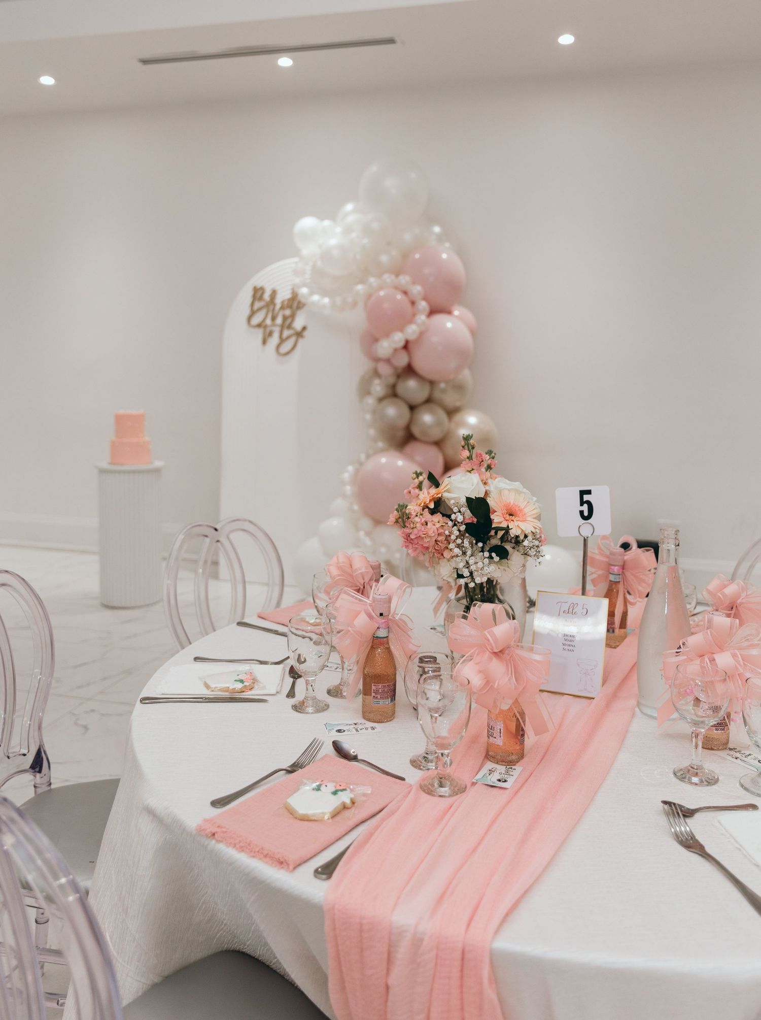 Modern wedding reception table with pink runner and clear ghost chairs.