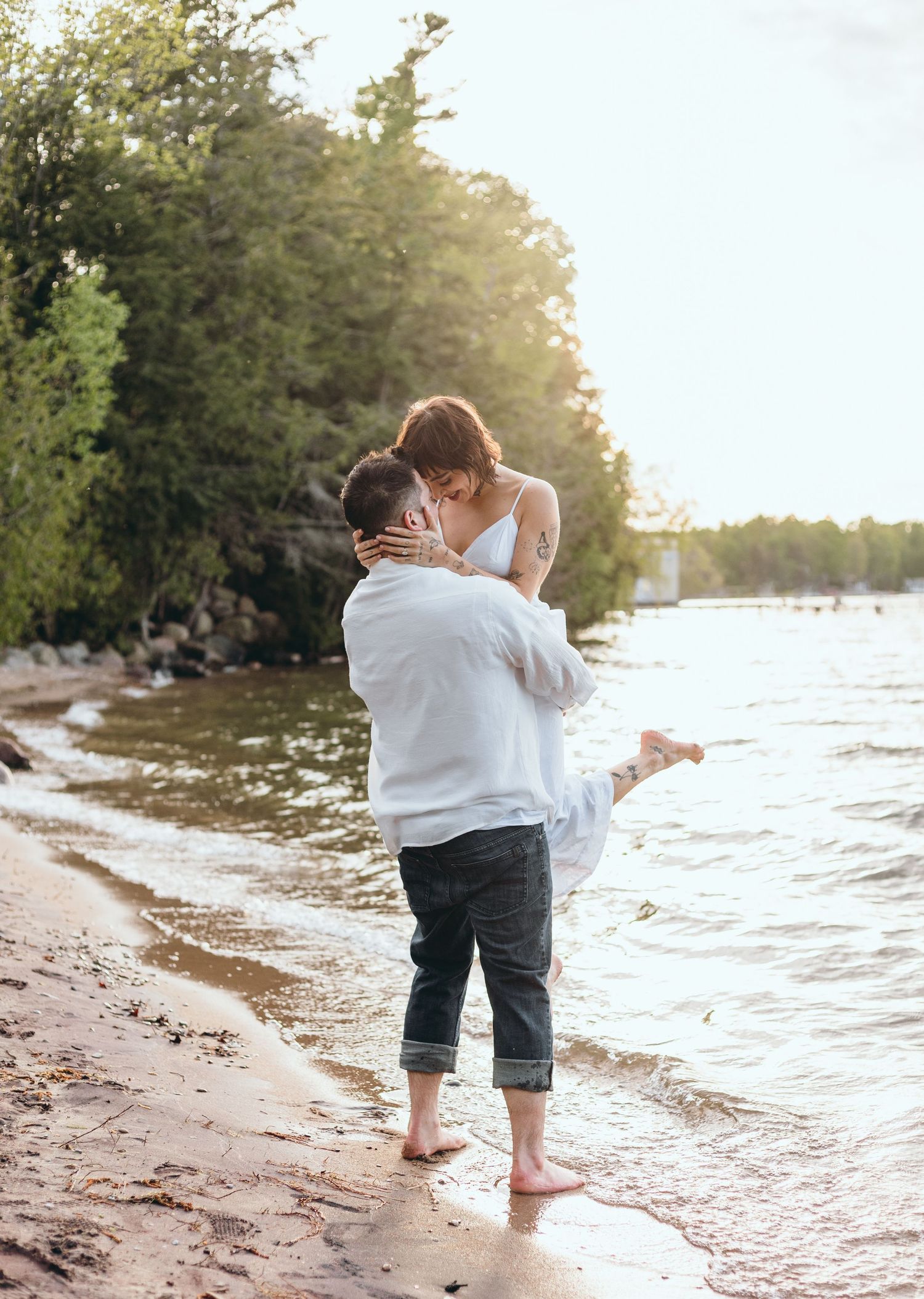 Romantic couple playing in shallow water at sunset on sandy beach.