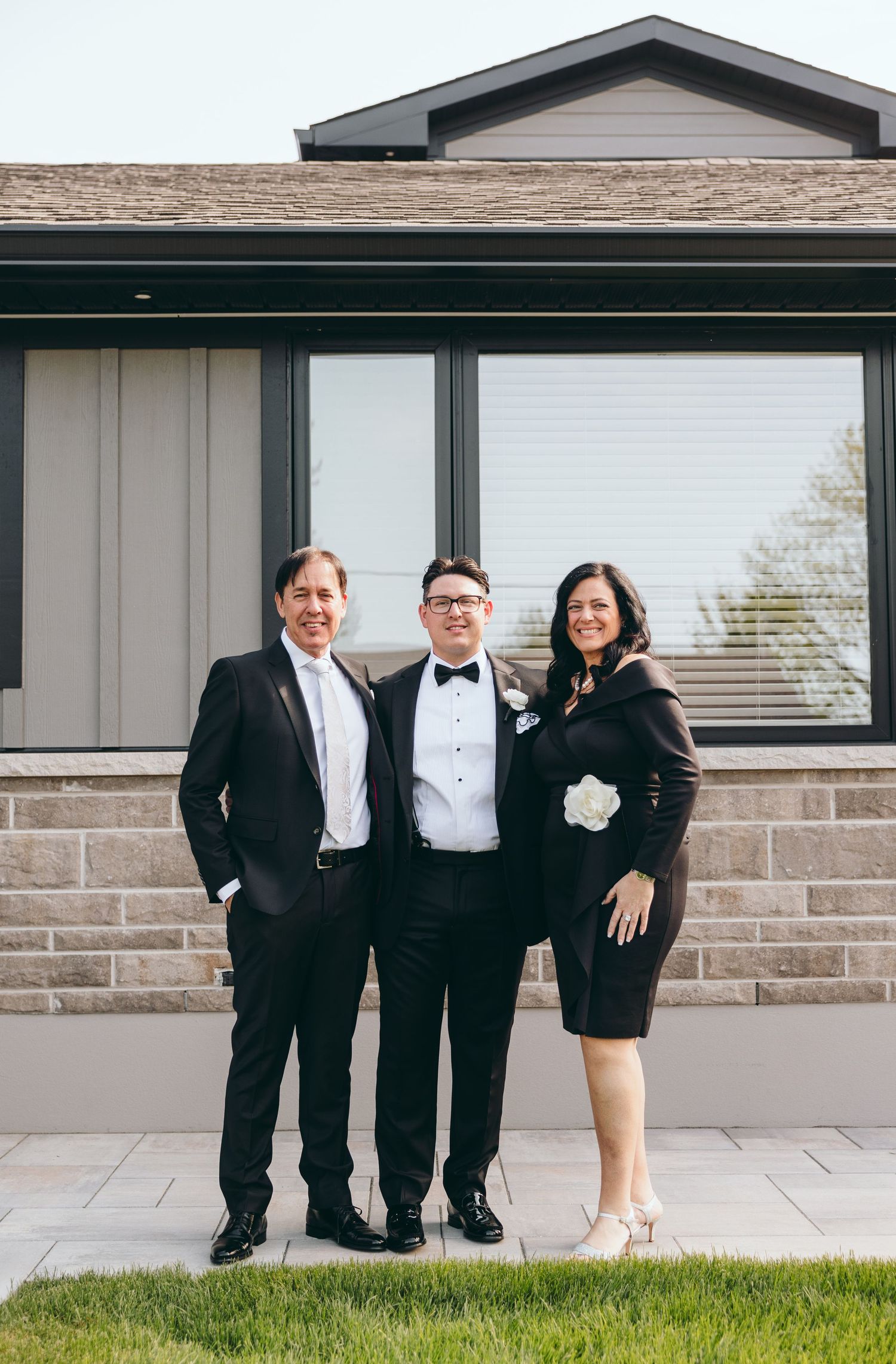 Small wedding party group poses outdoors against modern building with stone and glass features.