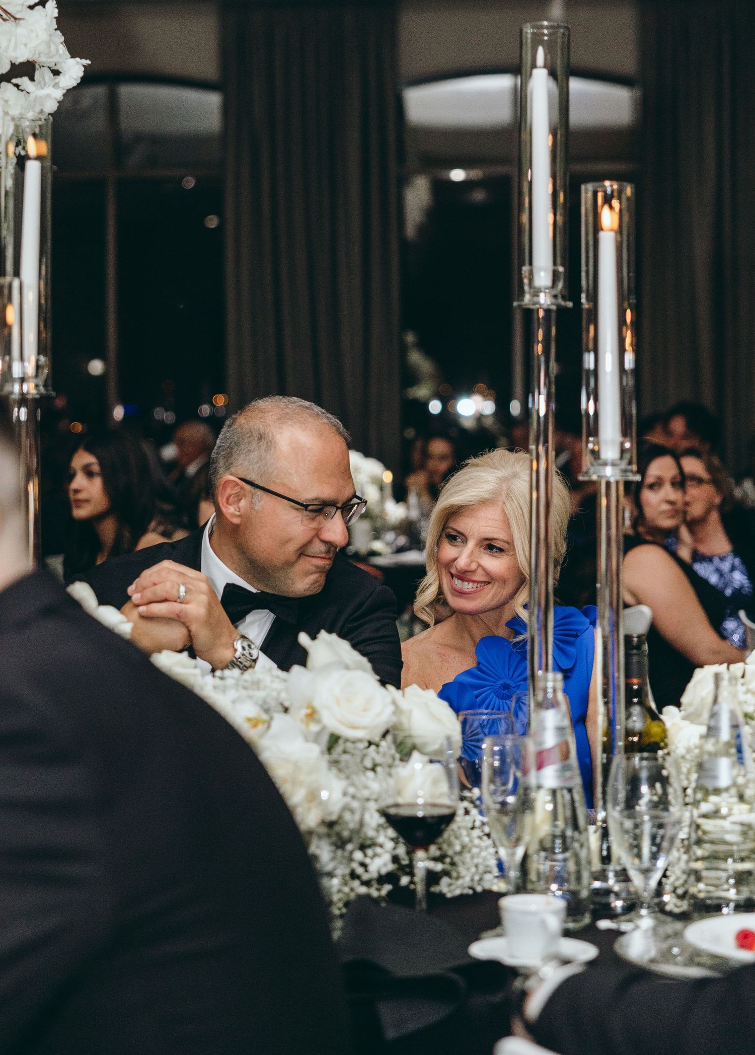 Elegant wedding reception with blue glassware and white floral centerpieces on dining tables.