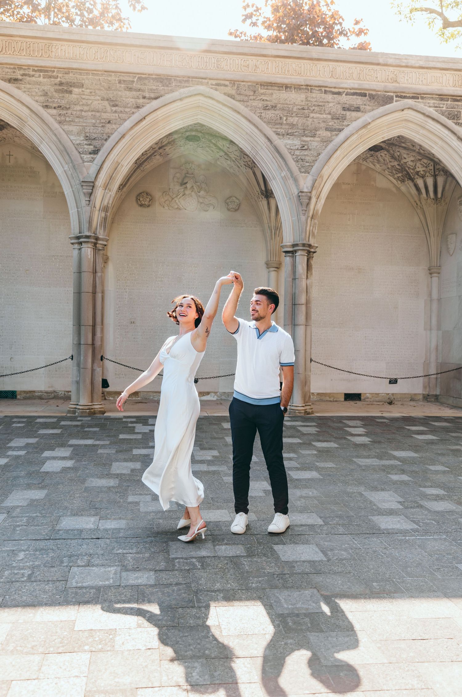 A couple performs a playful dance move under gothic stone archways.