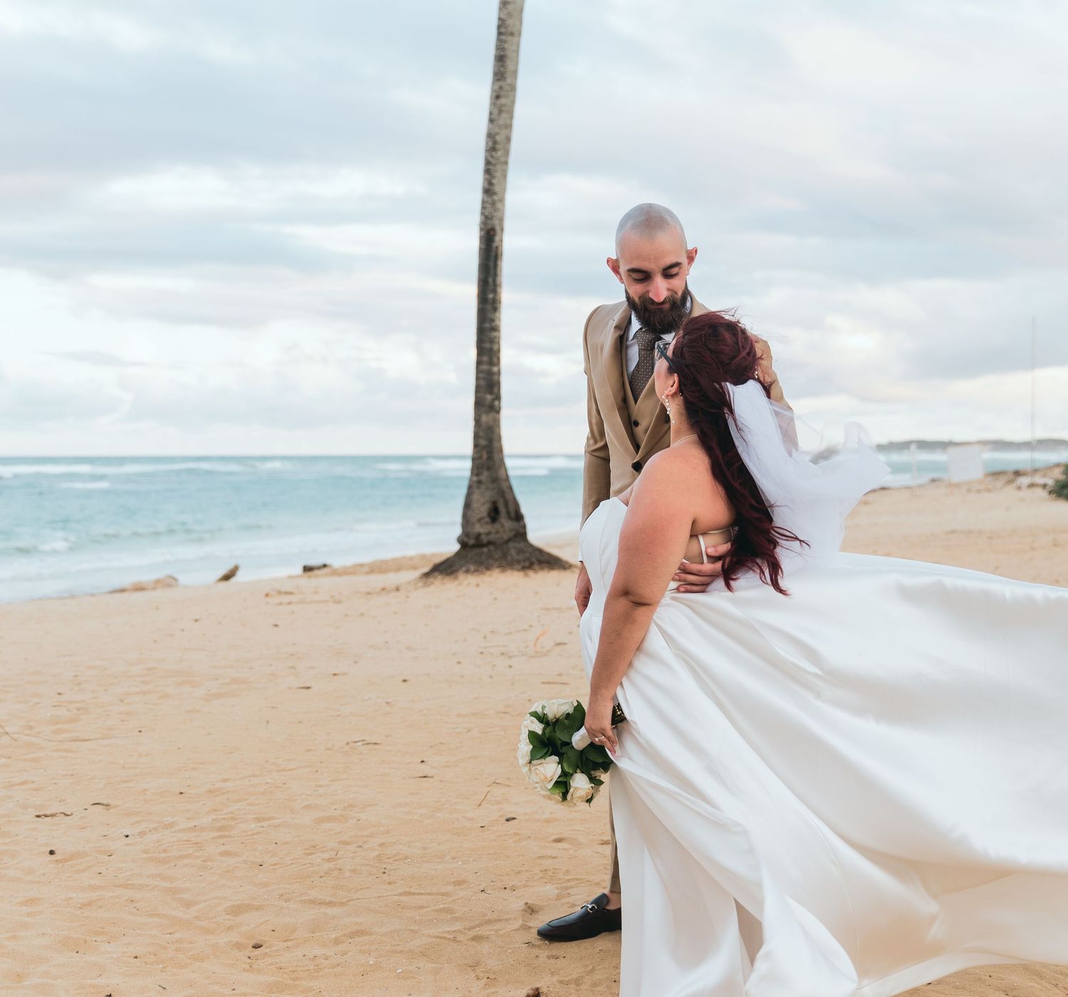 A flowing white wedding dress billows in the ocean breeze during a beach photoshoot.