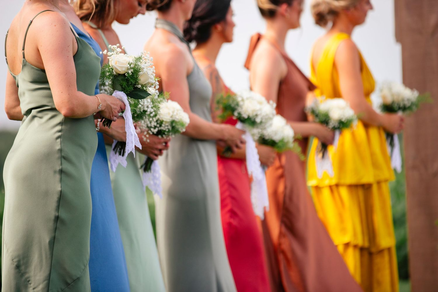 Bridesmaids in colorful dresses of yellow, red, blue and green holding white bouquets.