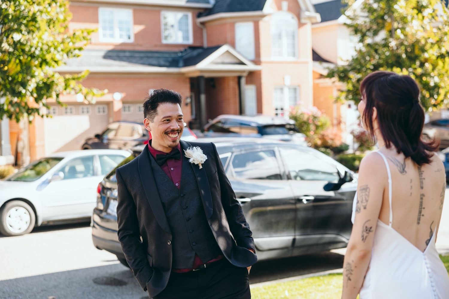 A candid moment between a couple in wedding attire outside a brick house.