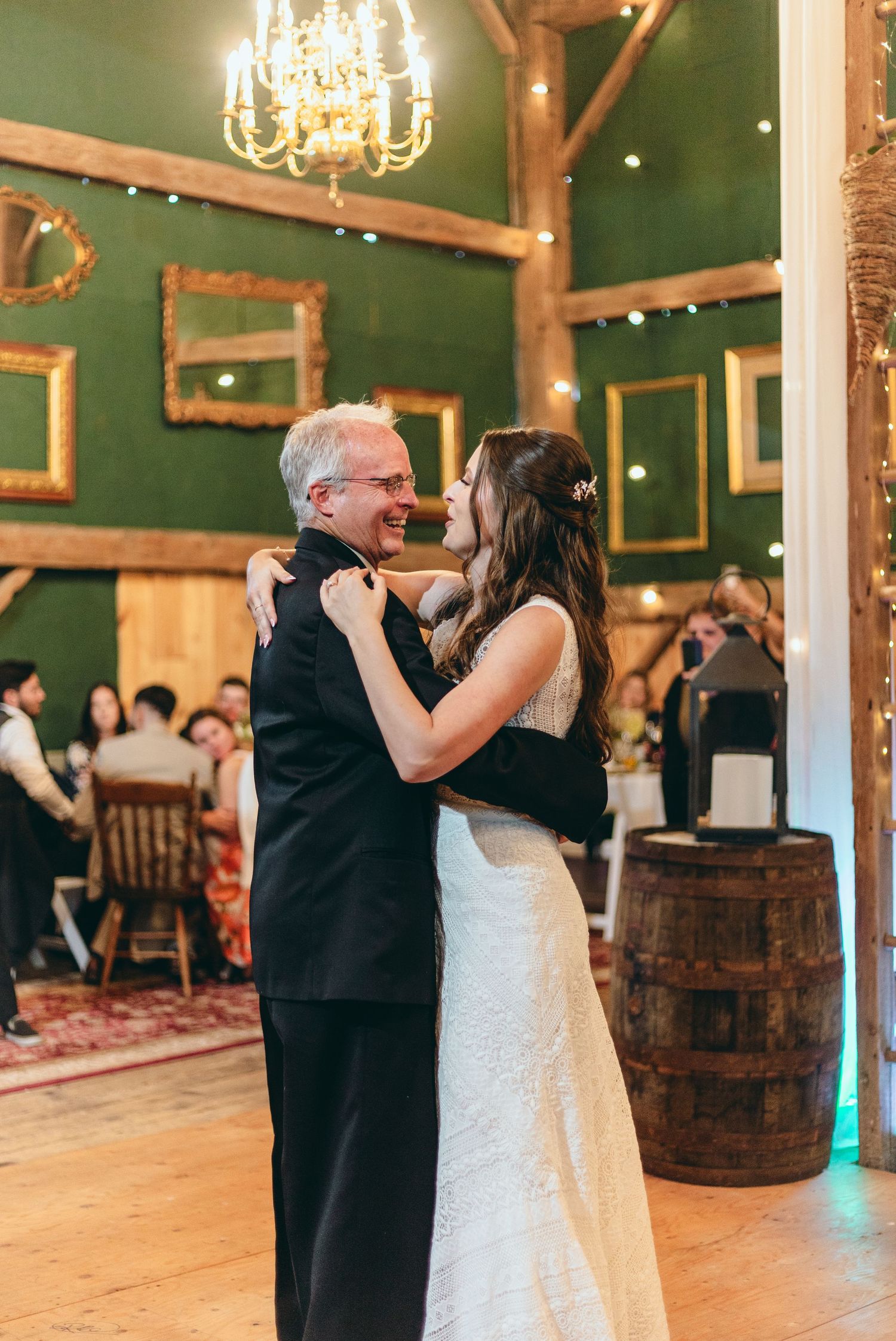 Couple dancing together in rustic barn venue with green walls and wooden posts.