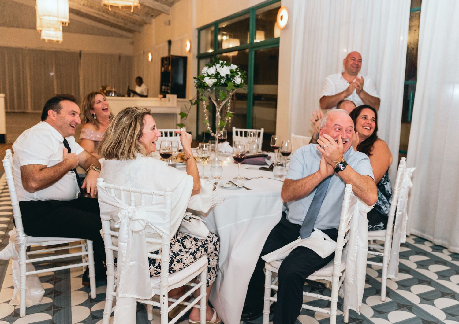 Wedding reception guests enjoying themselves at decorated round tables with white chairs.