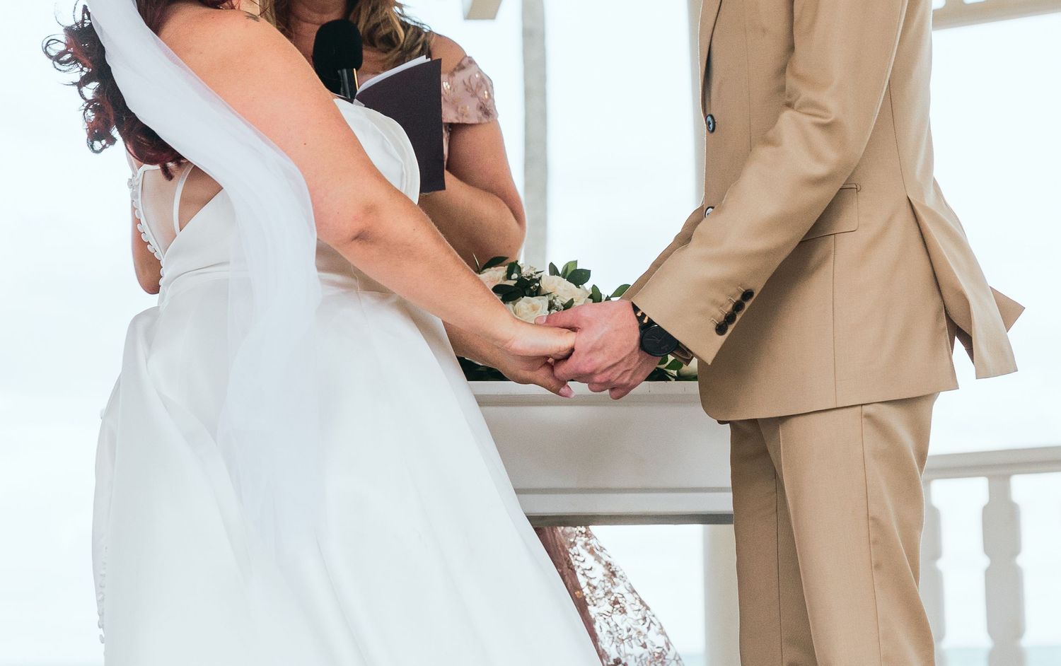 A couple shares an intimate moment during their beach wedding ceremony under a white gazebo.
