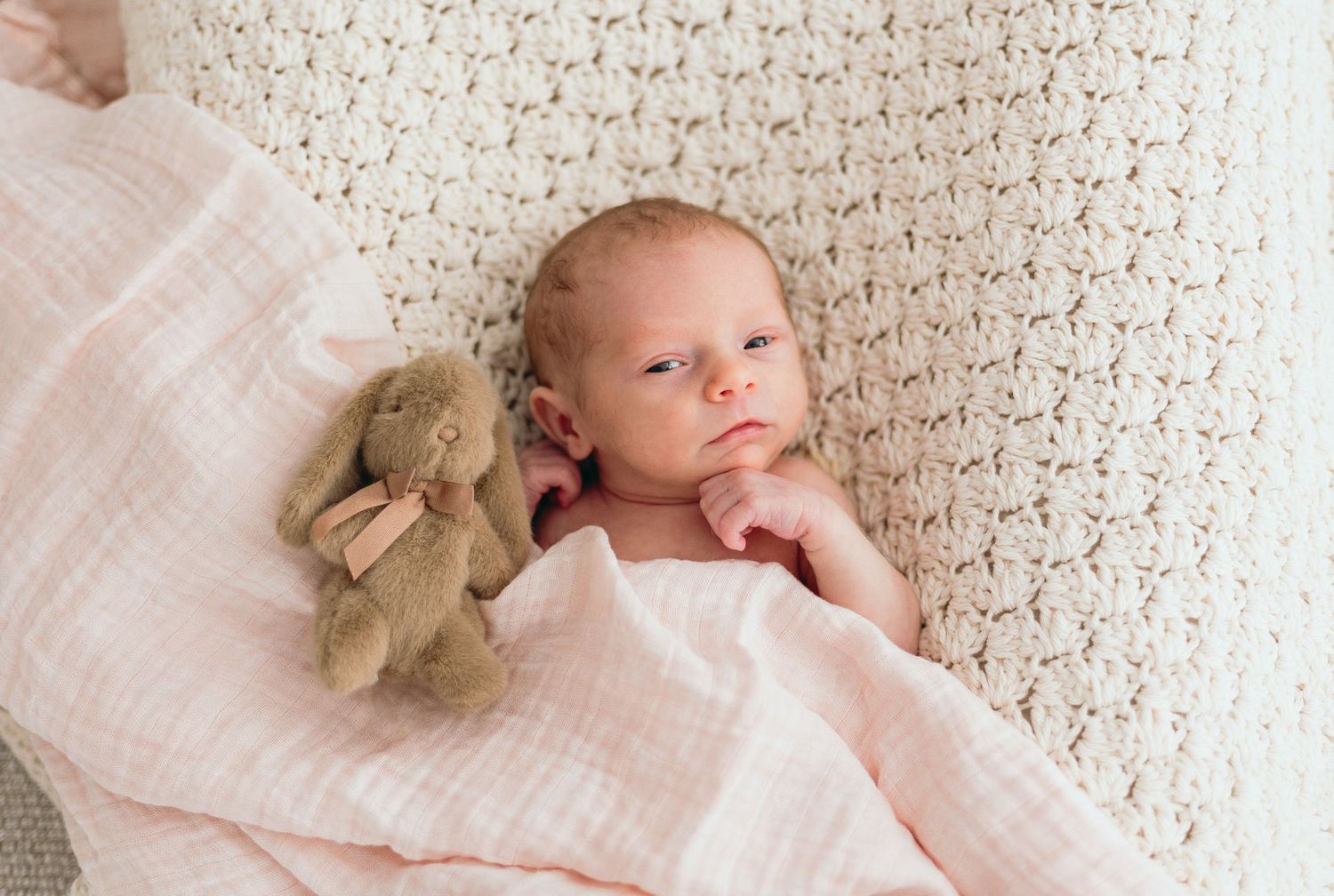 Newborn photography session featuring soft textures and neutral tones with plush toy detail.