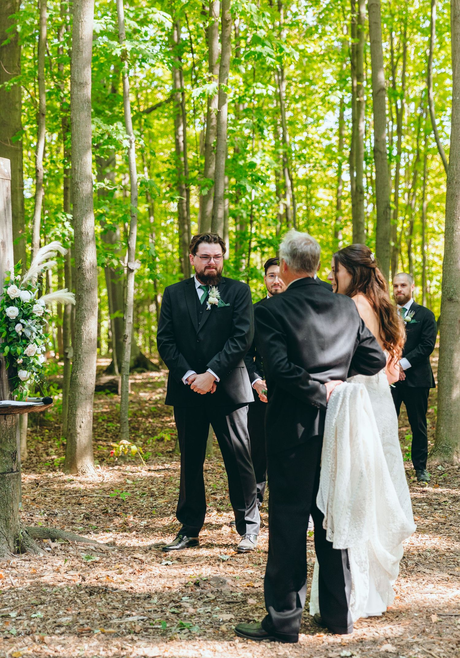 Wedding party gathered in a forest clearing wearing formal attire.