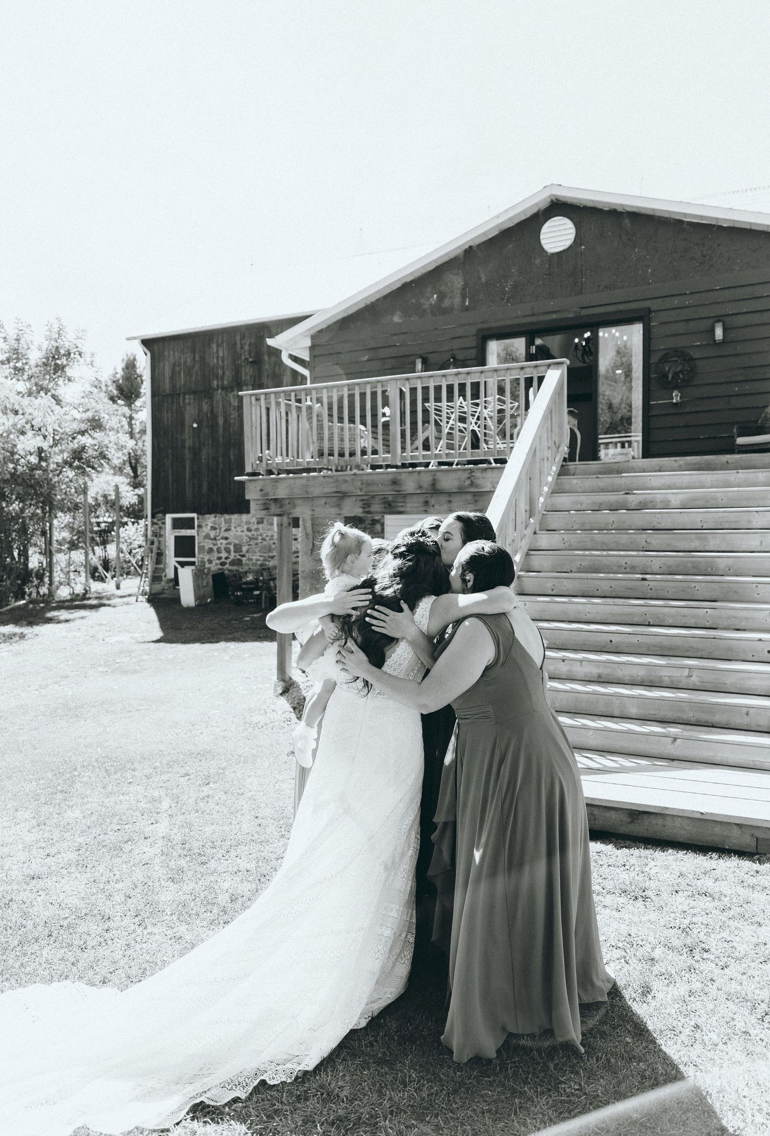 Wedding party members share drinks and laughter on rustic wooden steps of a venue building.