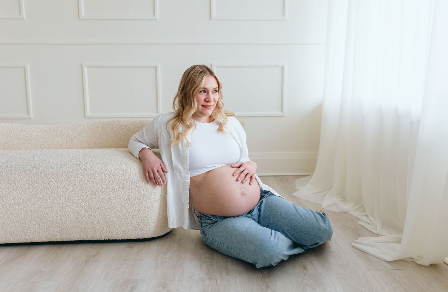 Maternity photo session in a bright minimalist studio with soft natural lighting.