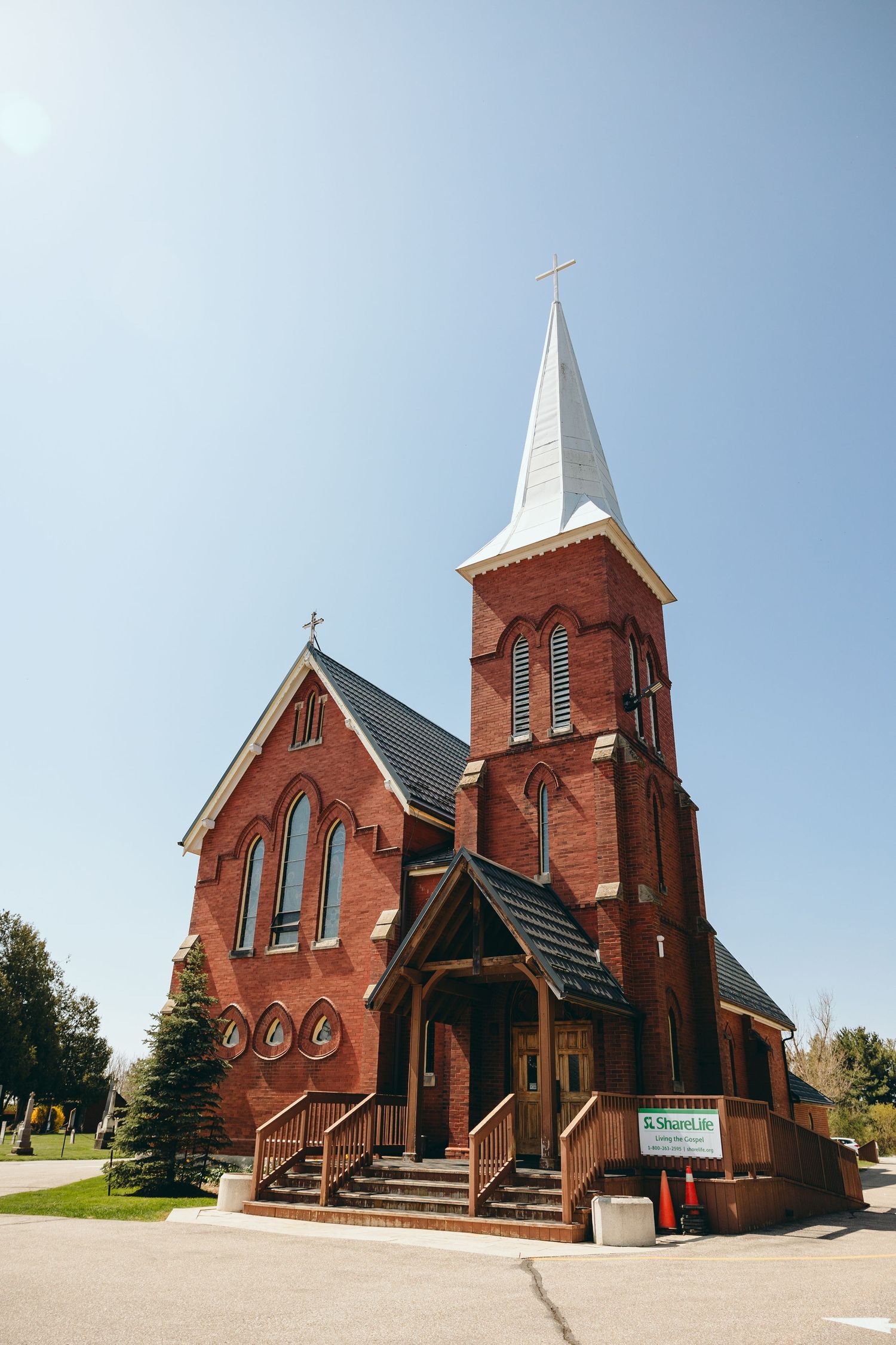 A red brick Gothic-style church with white steeple stands against a bright blue sky.