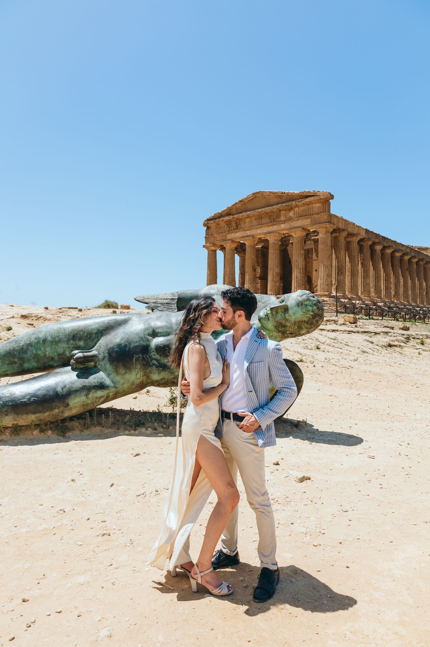 A couple poses romantically against ancient Greek temple ruins and fallen statues in Sicily.
