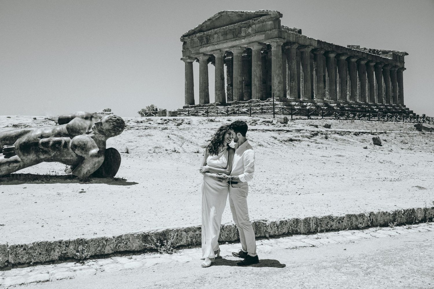 Two people share a romantic moment near historic Greek ruins in vintage photography.