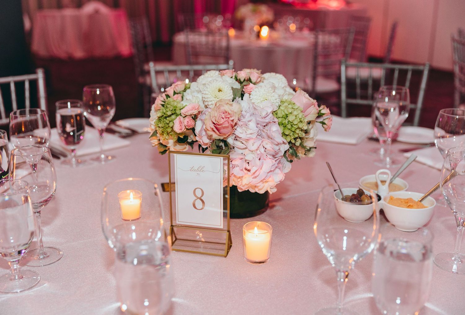 Elegant wedding reception table setting with pink lighting and candle centerpieces.