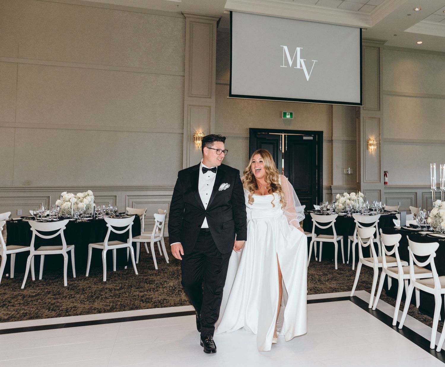 Newlyweds walking together in formal attire through elegant reception venue.