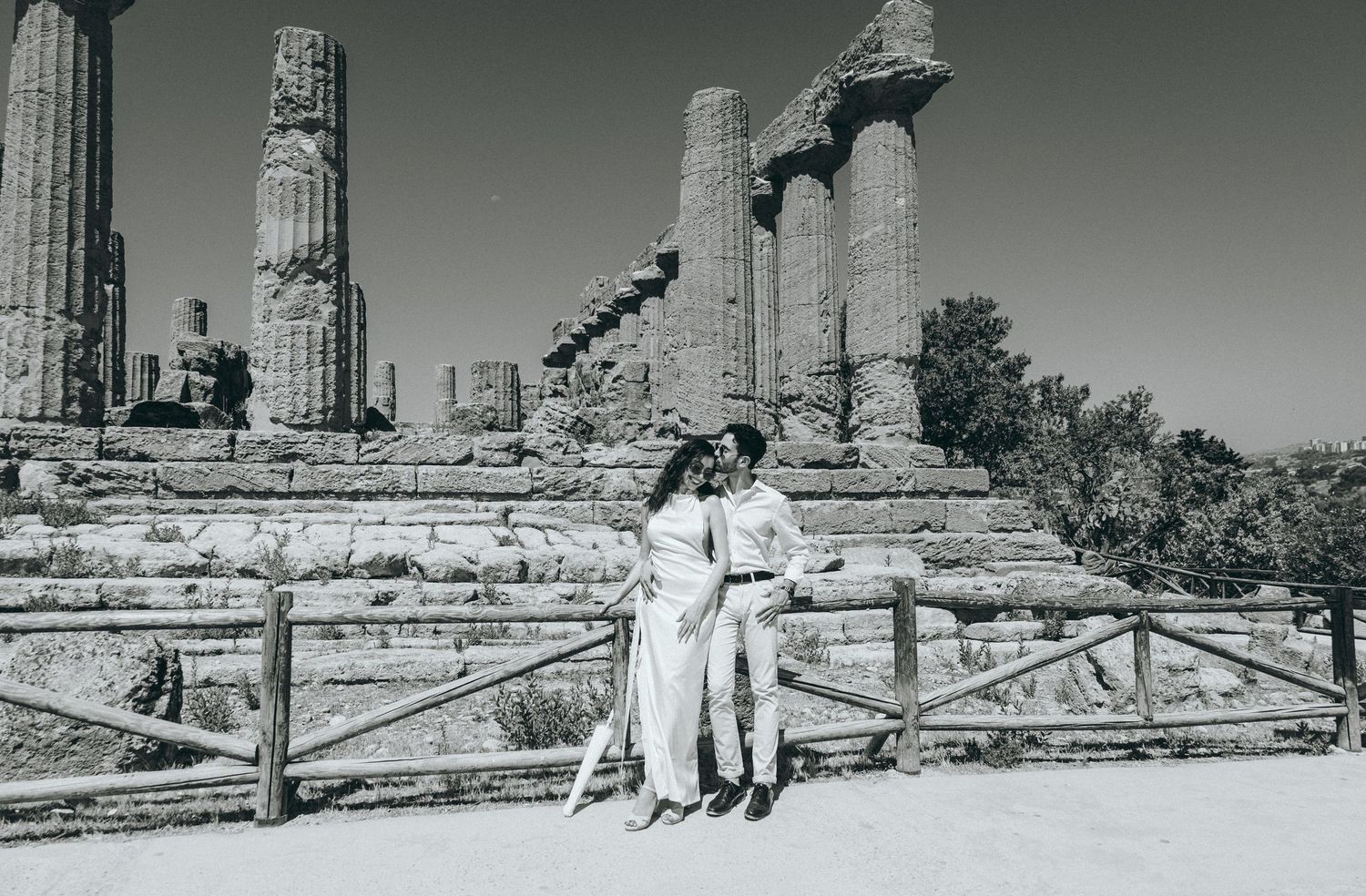 Monochrome panoramic view of ancient temple ruins with wooden fence in foreground.