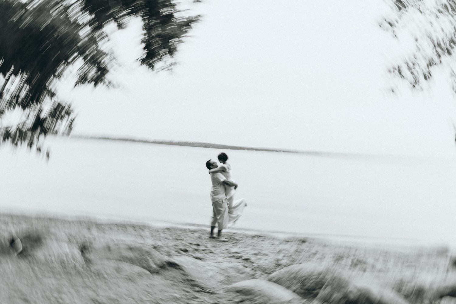 Artistic blurred black and white photo of couple embracing by water.