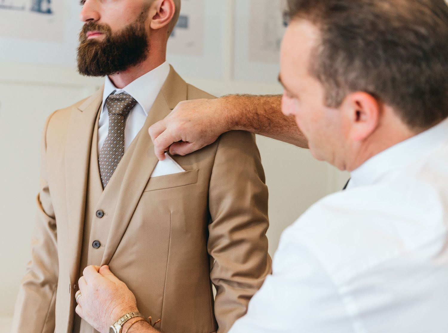 Men in tan suits and white shirts engage in conversation during formal event preparations.