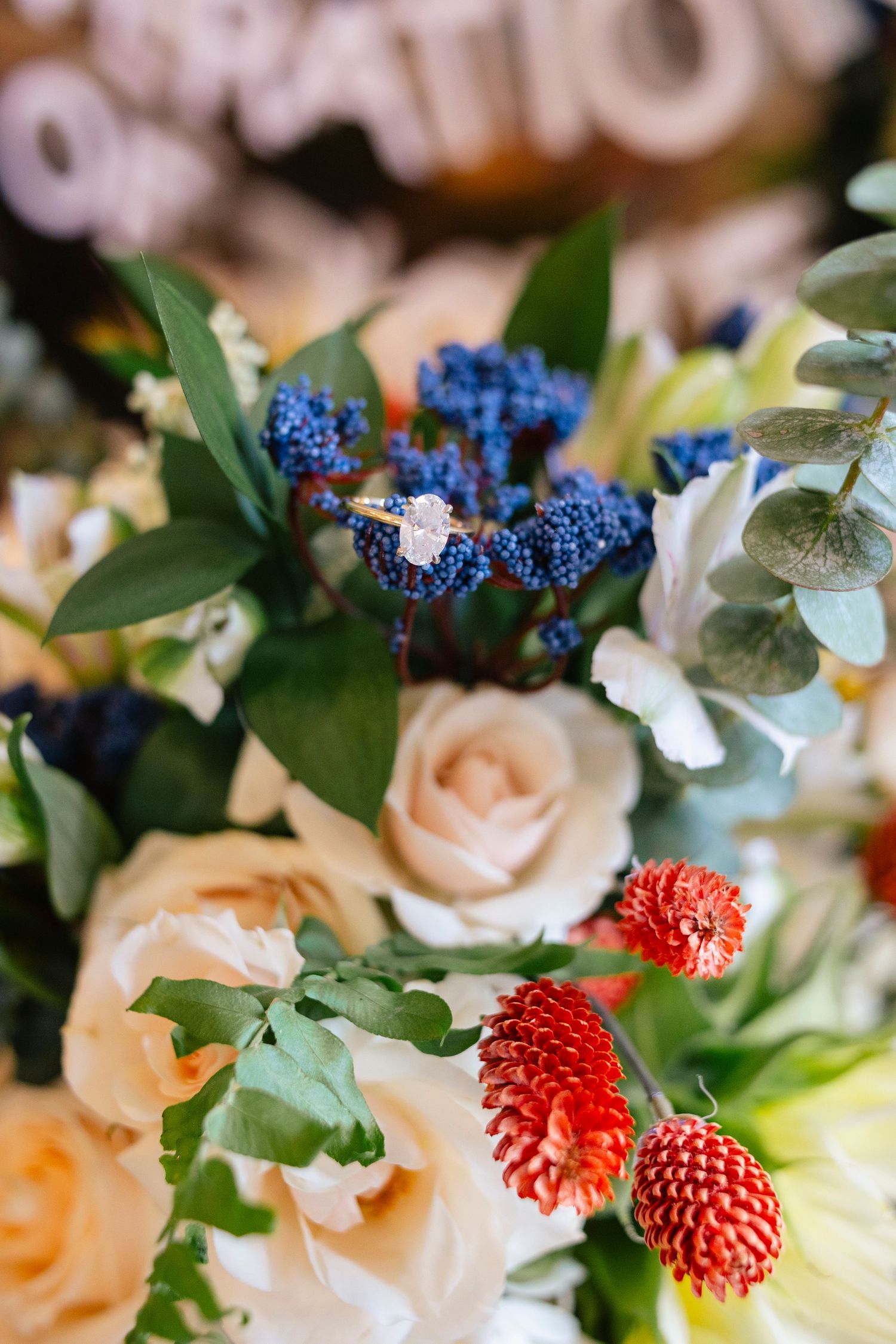 Elegant wedding bouquet featuring blue flowers, peach roses, and red blooms with green foliage.