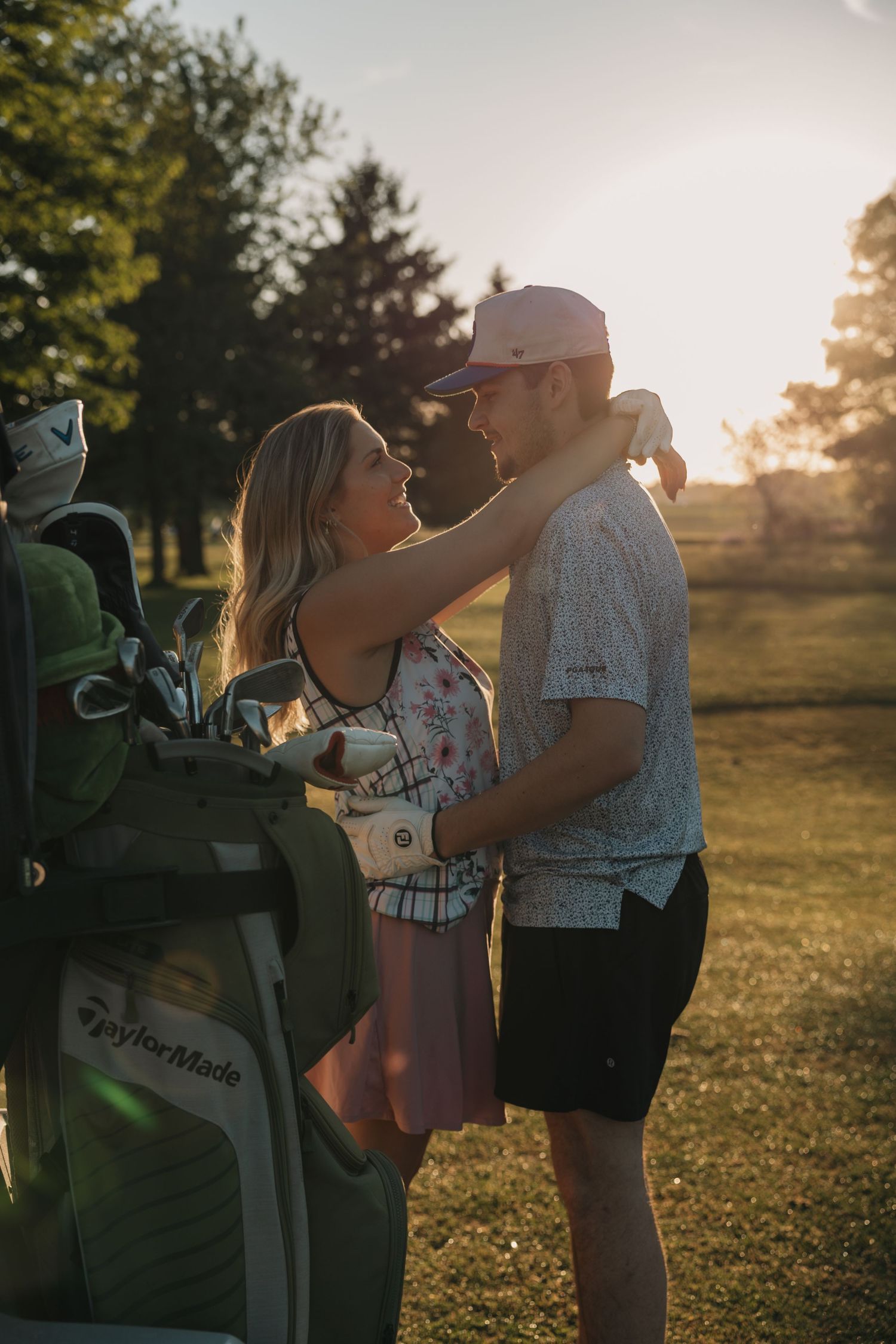 Romantic couple embracing on a golf course at golden sunset near a TaylorMade golf bag.