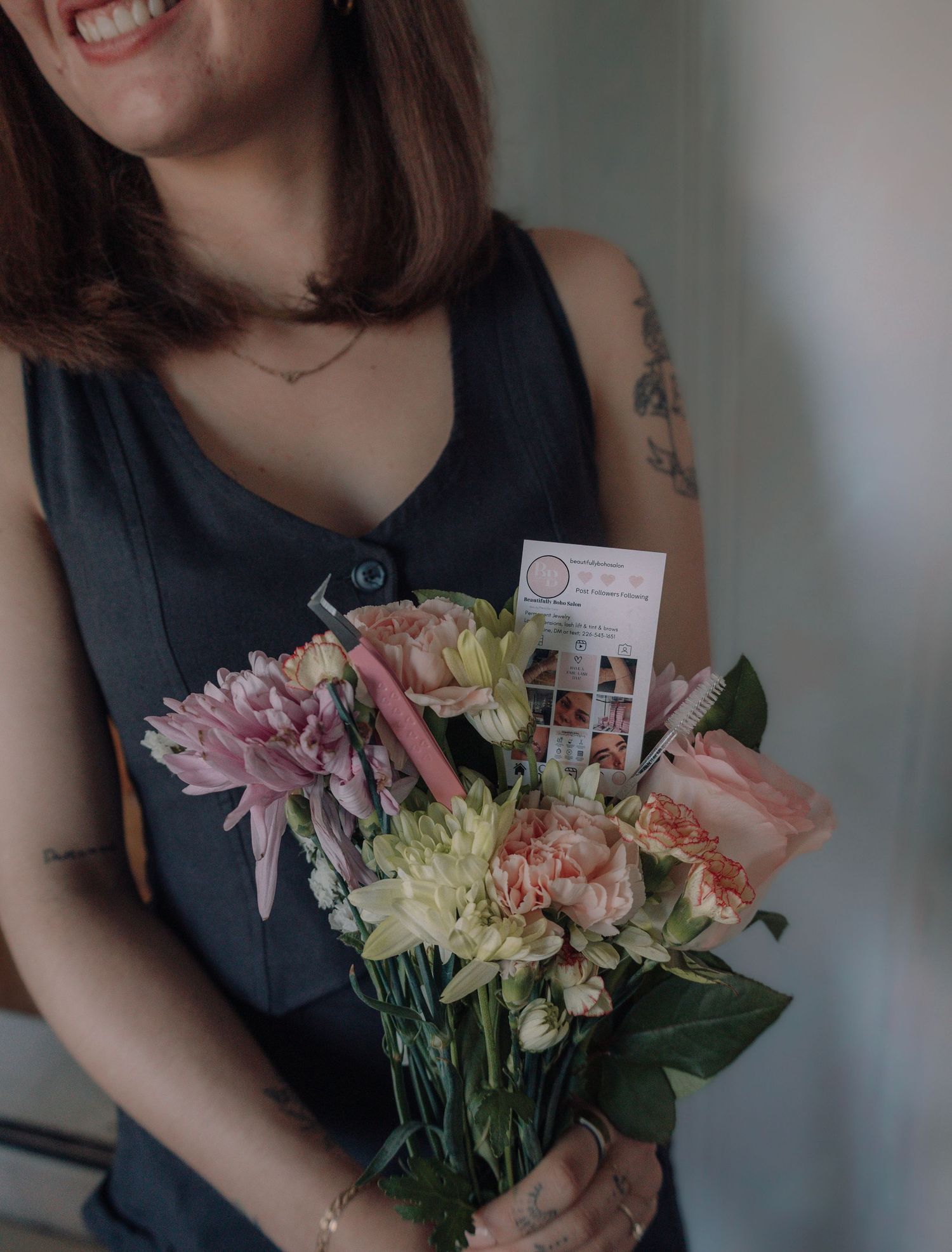 Woman in gray top holding a bouquet of pink and cream flowers with a business card.