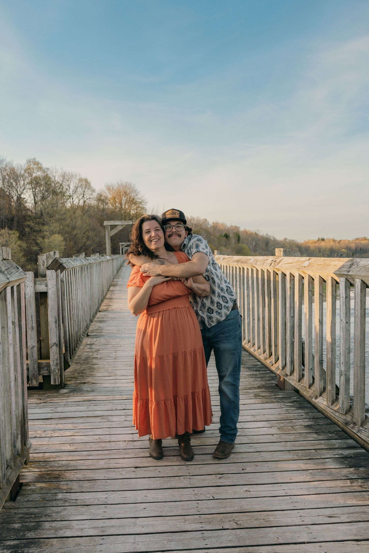 Mom and son on a wooden bridge at sunset, woman in orange dress.