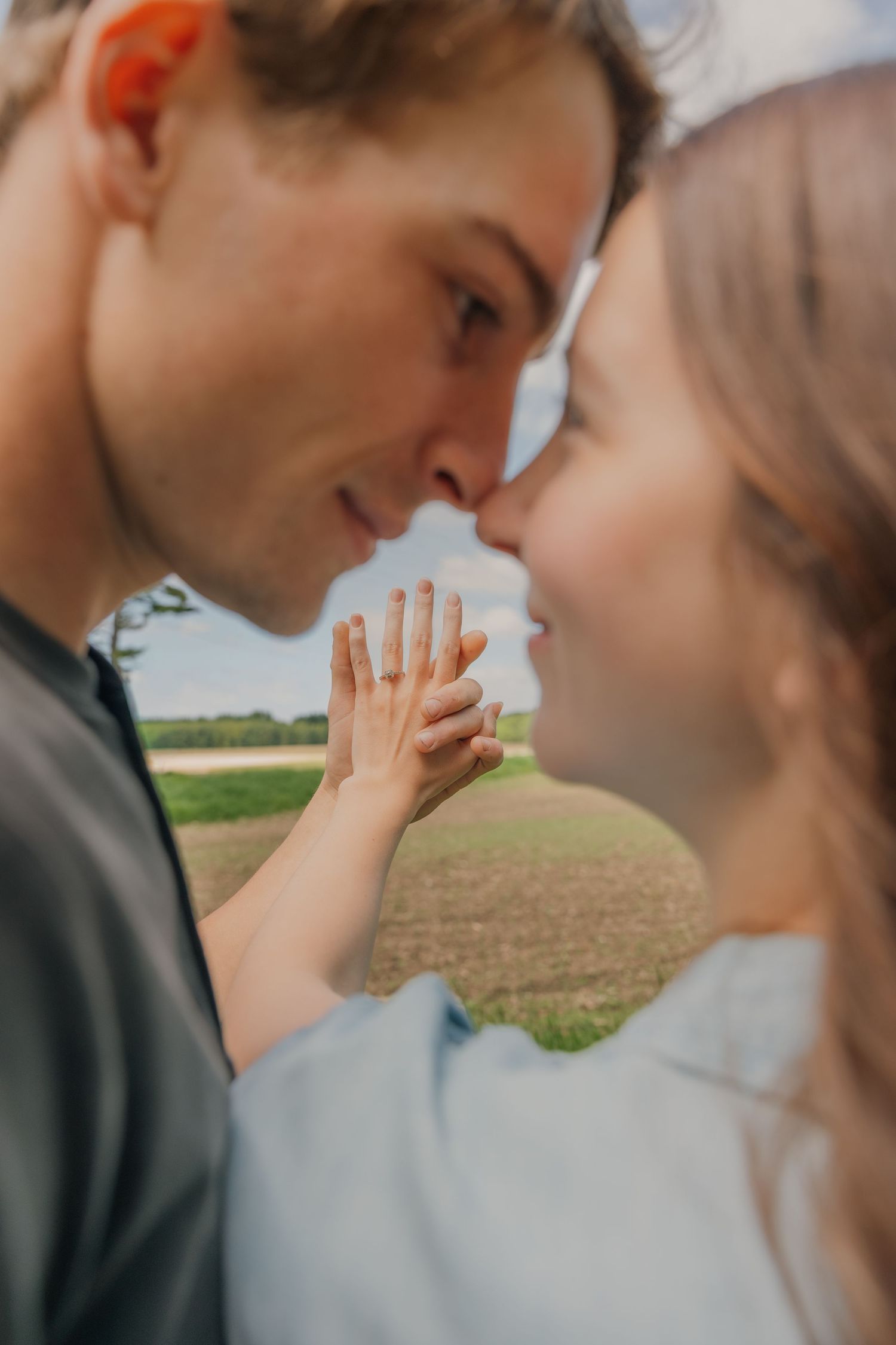 Close-up of engaged couple nearly kissing while woman shows off her diamond engagement ring.