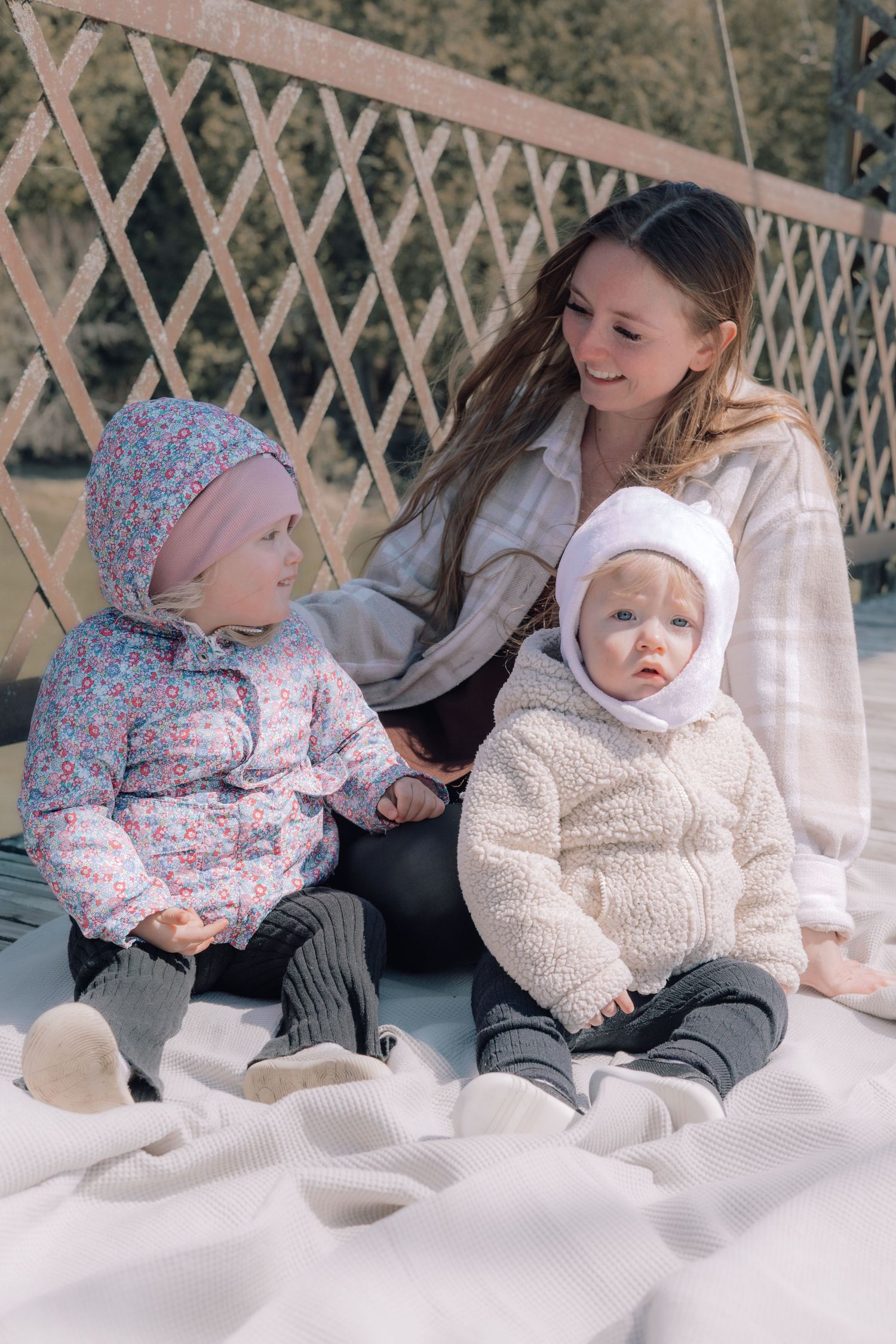 Young mother sitting on a blanket with two toddlers on a sunny bridge.