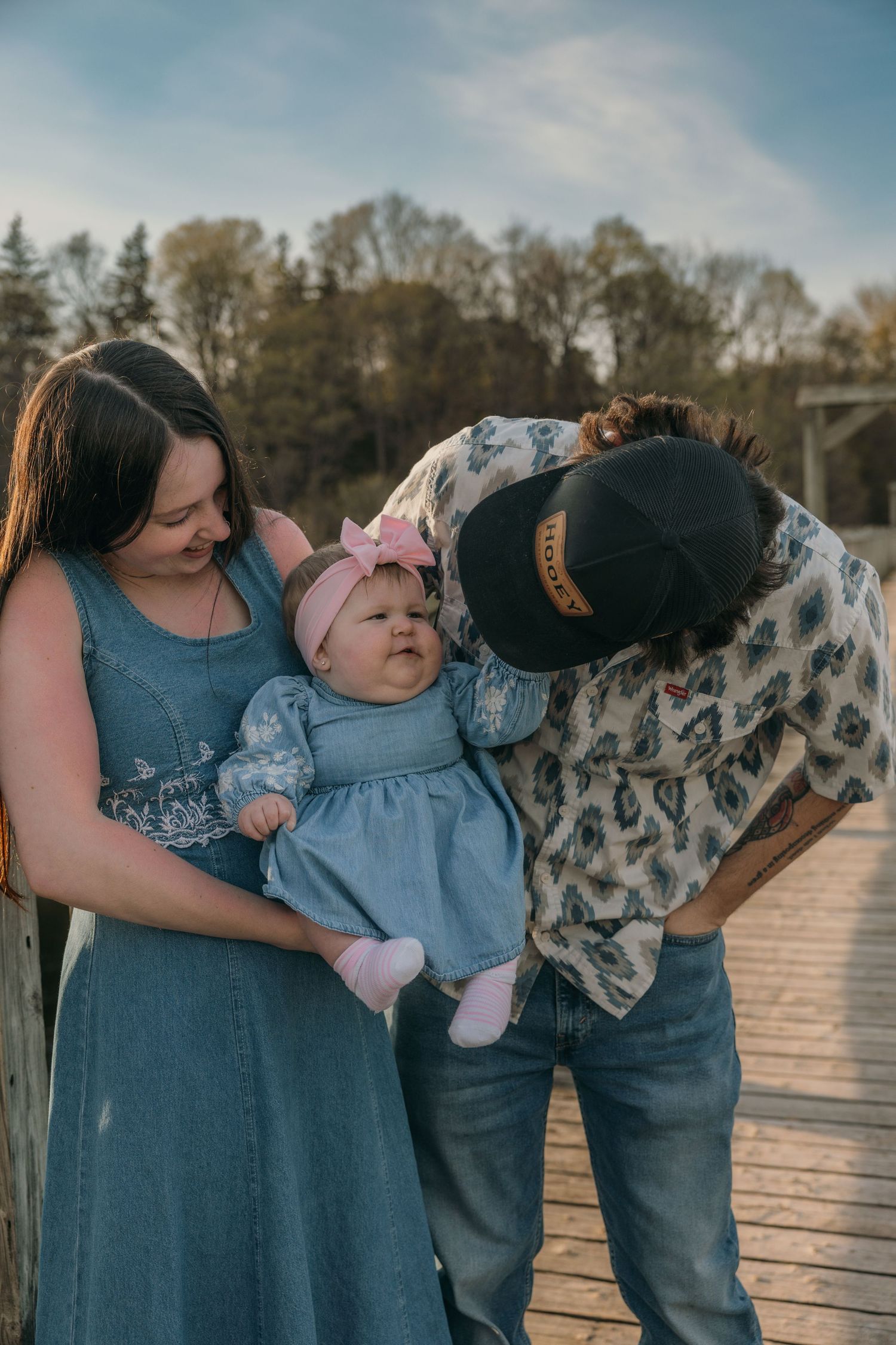 Parents lovingly attending to their baby girl in a blue dress on a bridge.