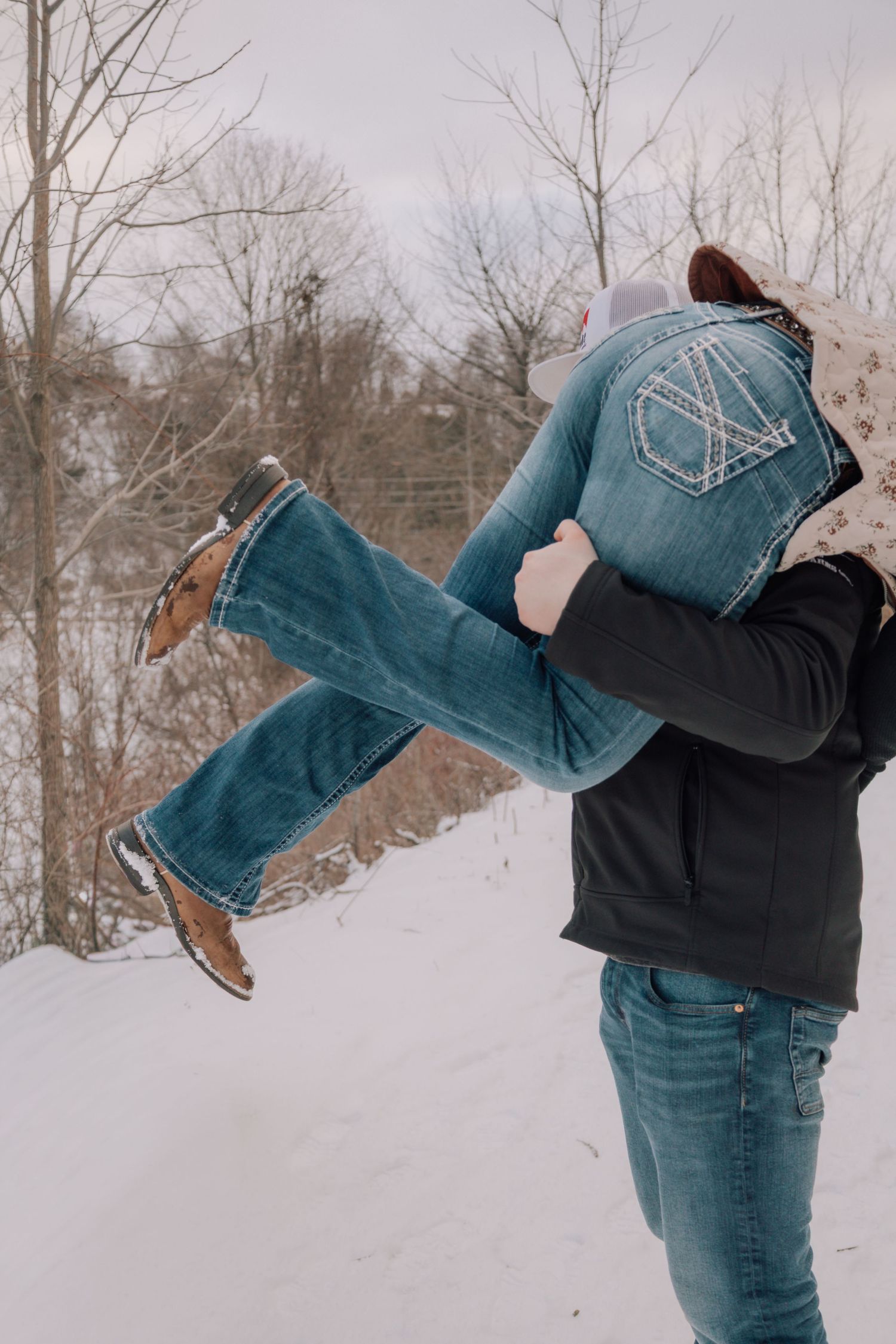 Man playfully lifting woman over his shoulder in a snowy winter landscape.