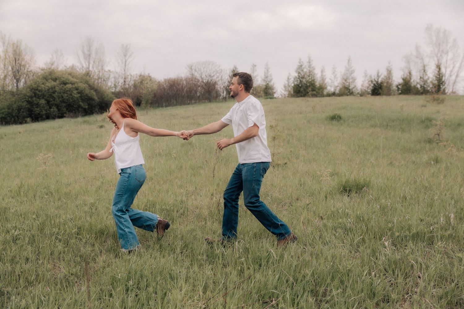 A joyful couple holds hands while running together through a wide open green grassy field.
