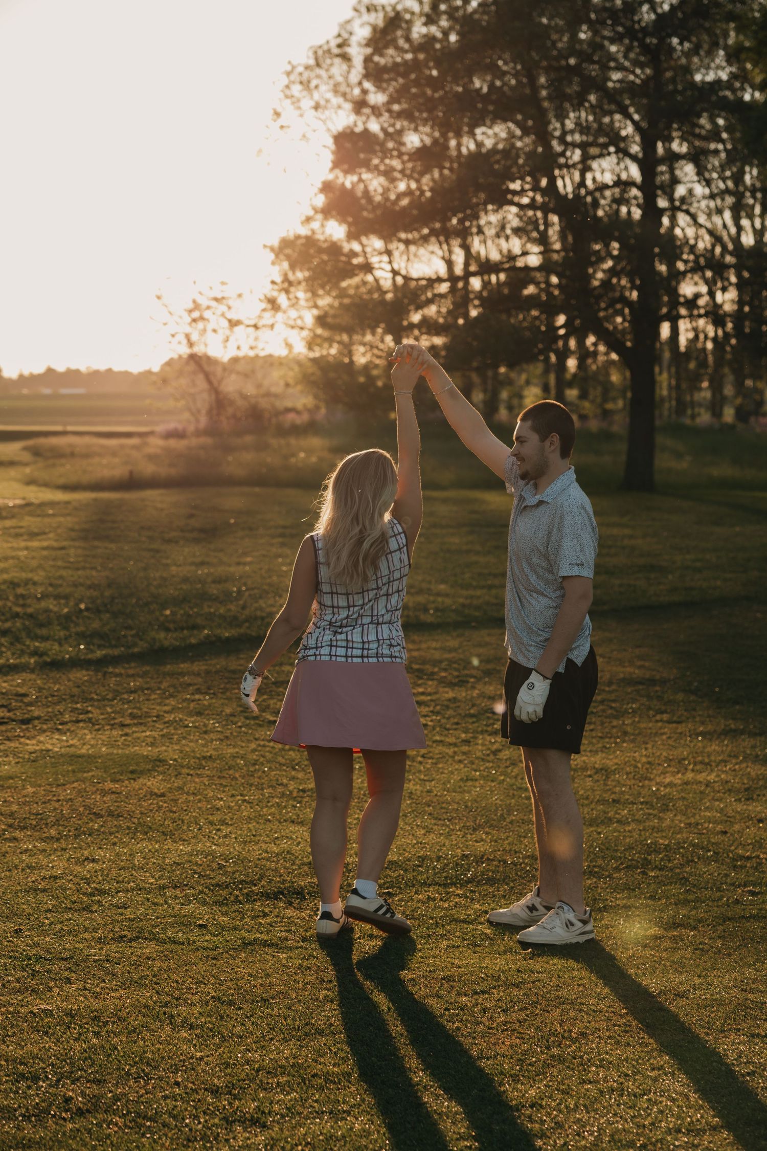 Couple holding hands and spinning together on a lush golf course at golden hour sunset.