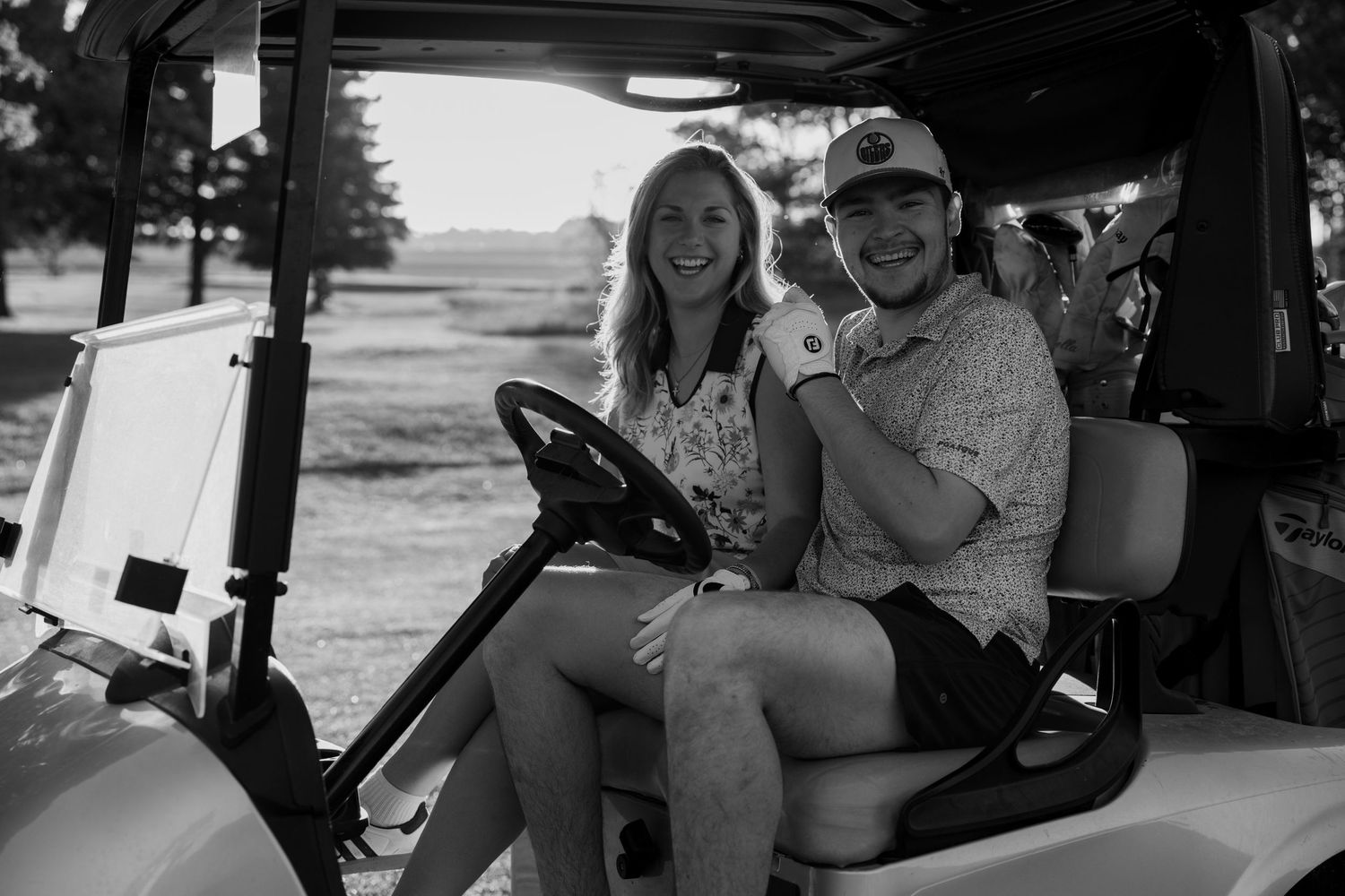 Smiling couple sitting together in a golf cart on a sunny course.
