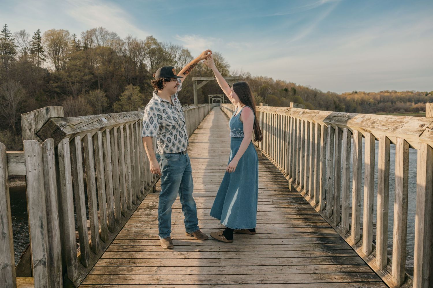 A couple dances on a wooden bridge boardwalk with trees in the background.